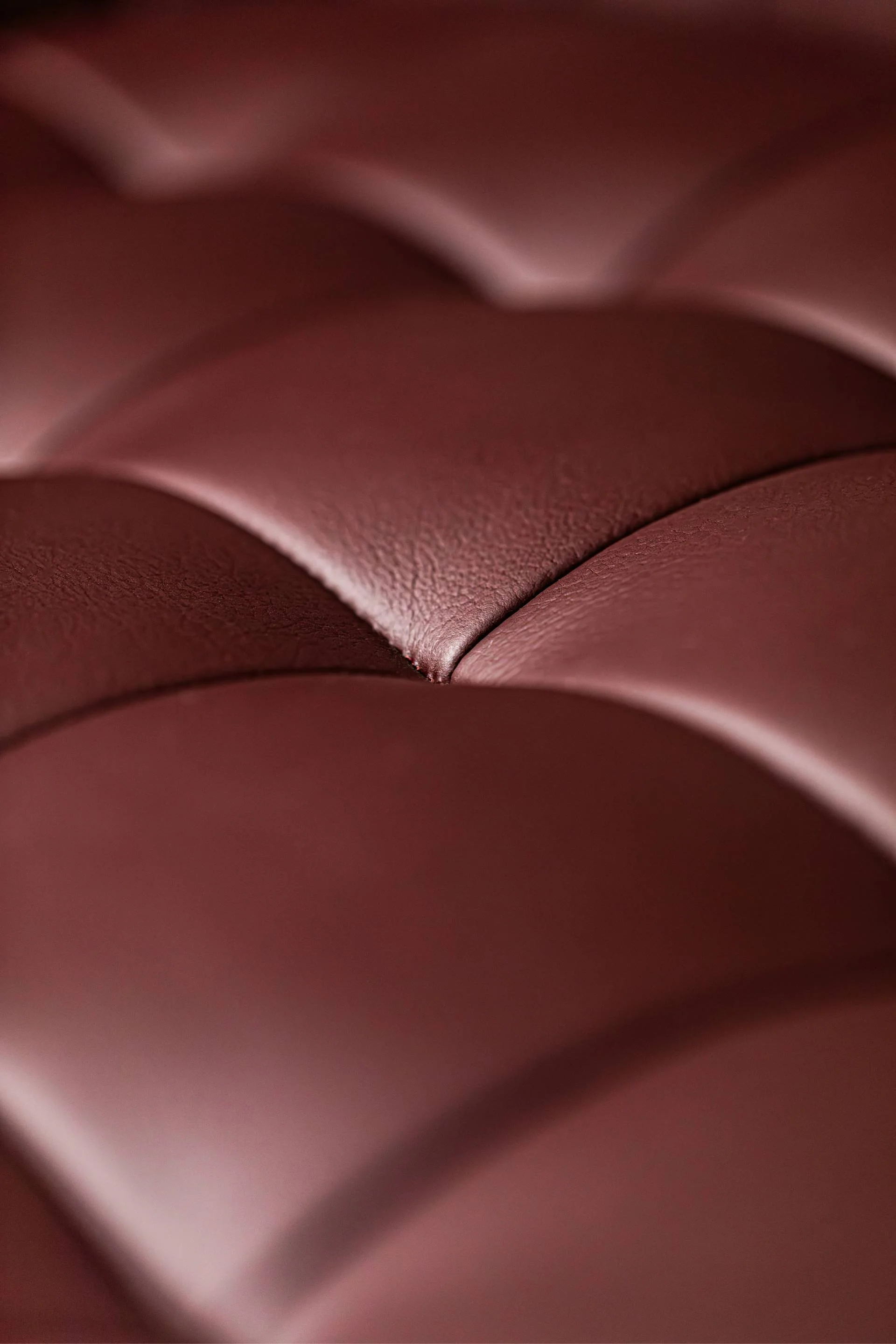 Close-up of a textured, burgundi leather surface with curved seams.