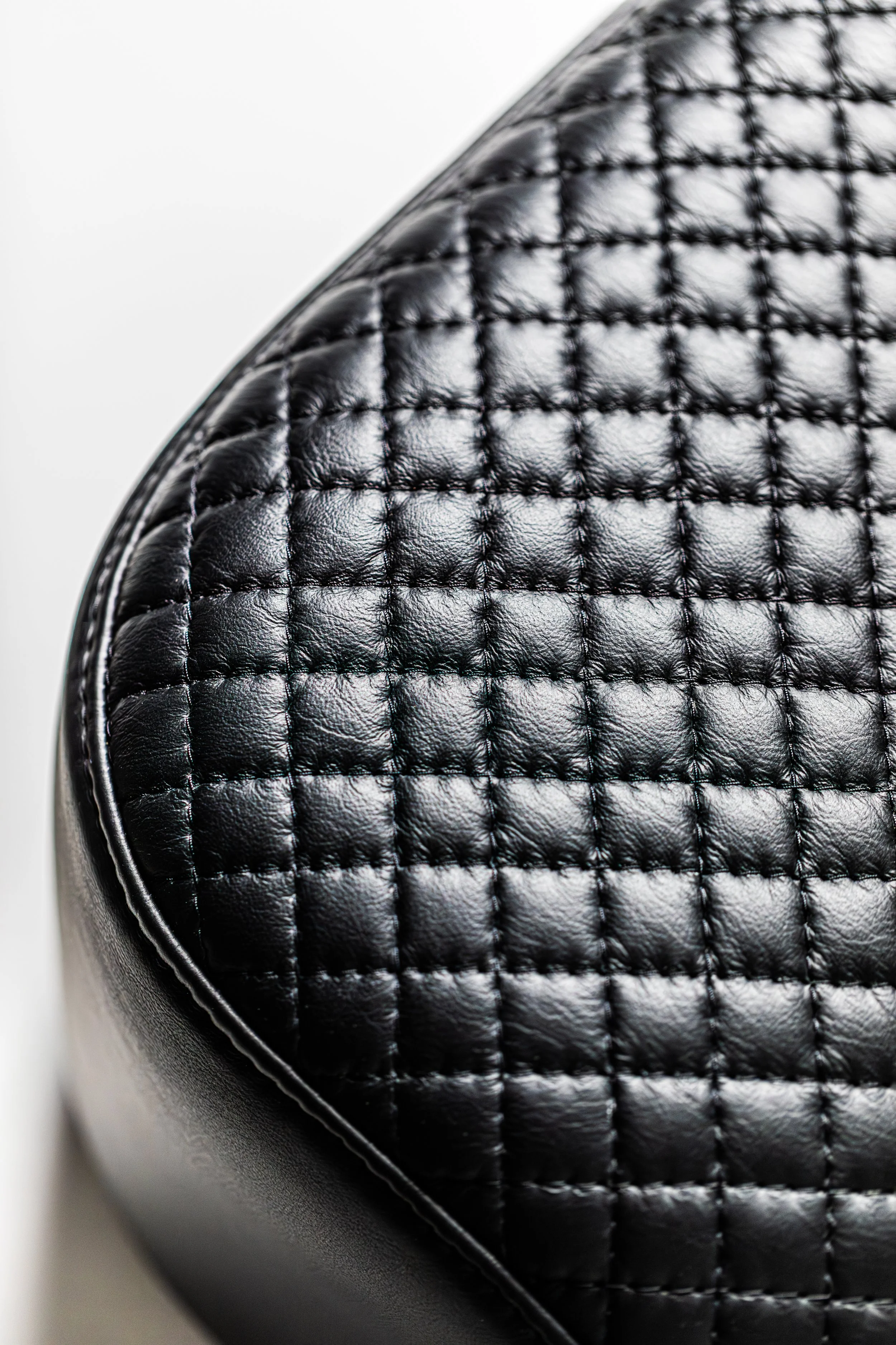 Close-up of black quilted leather material with a shiny finish, showing detailed stitching and texture.