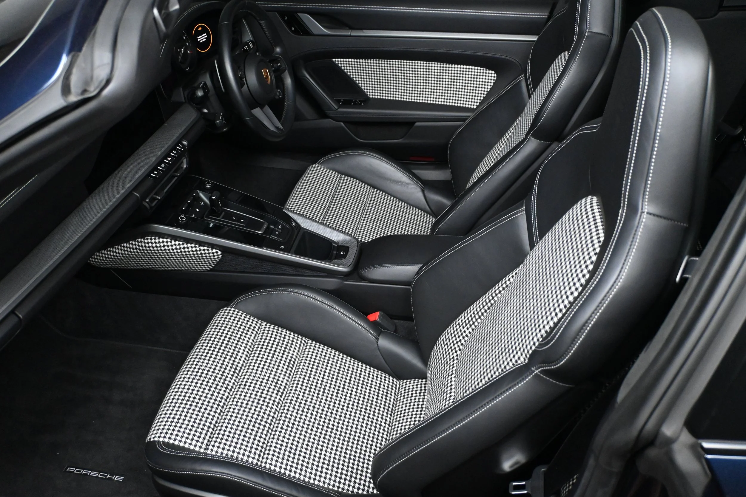 The interior of a luxury Porsche sports car, featuring black leather seats with chequered fabric inserts, a sleek dashboard, and a centre console with various controls.