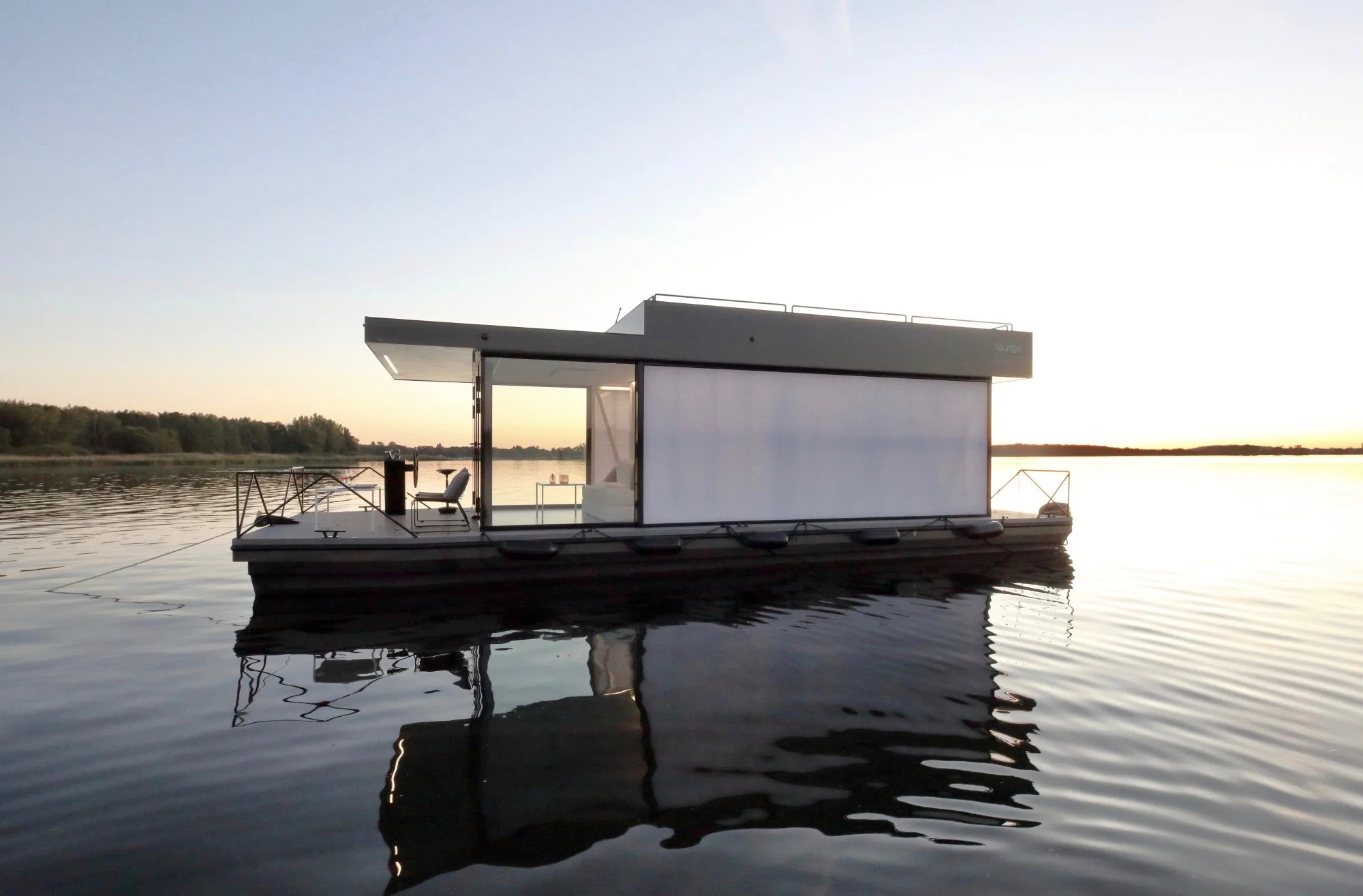 Ein moderner Hausboot auf ruhigem Wasser bei Sonnenuntergang, mit einer offenen Terrasse und minimalistischer Architektur.