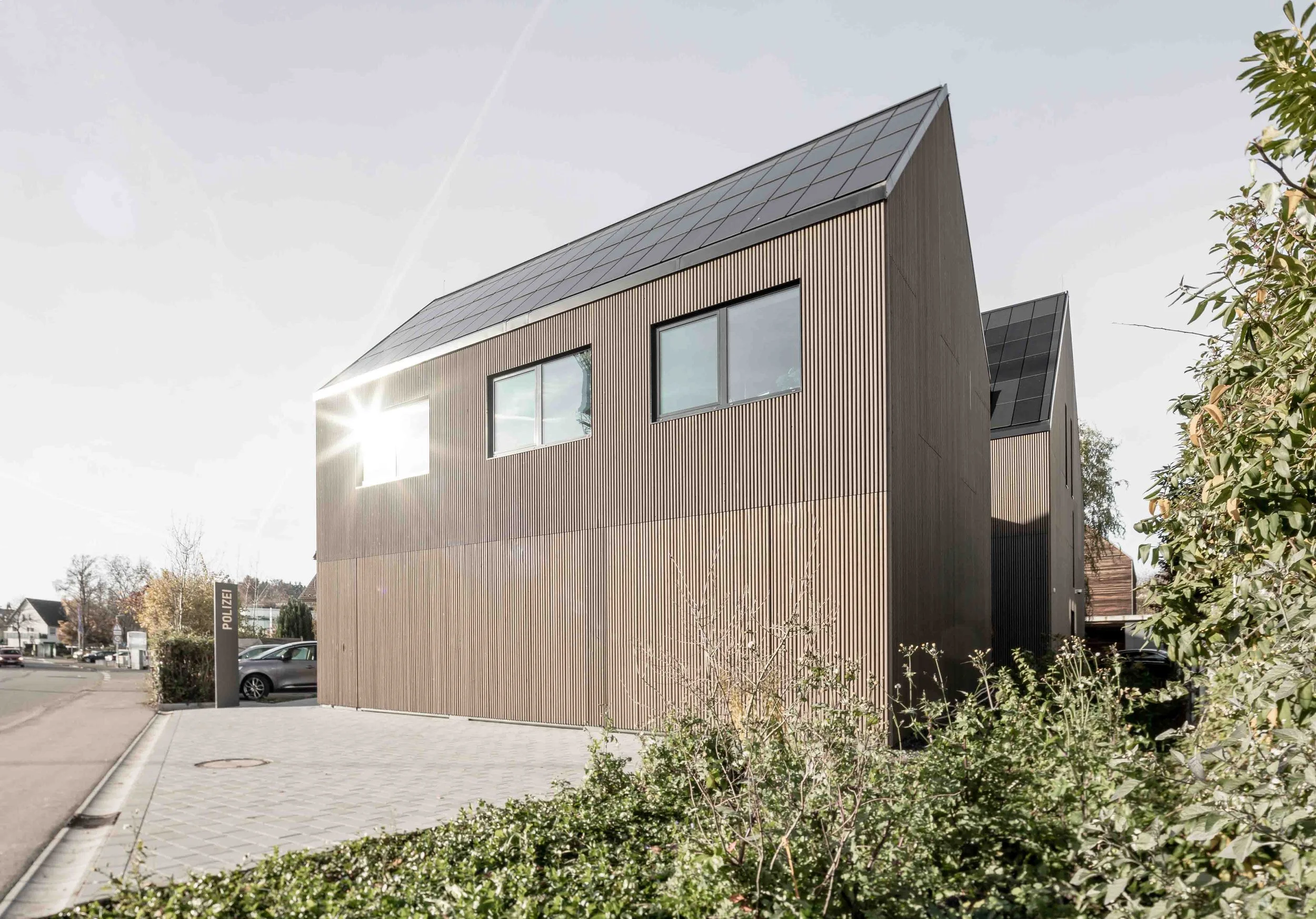 polizeiposten LE - Moderne, zweigeschossige Holzarchitektur mit großen Fenstern und Solardach, umgeben von Bäumen und einem Parkplatz.