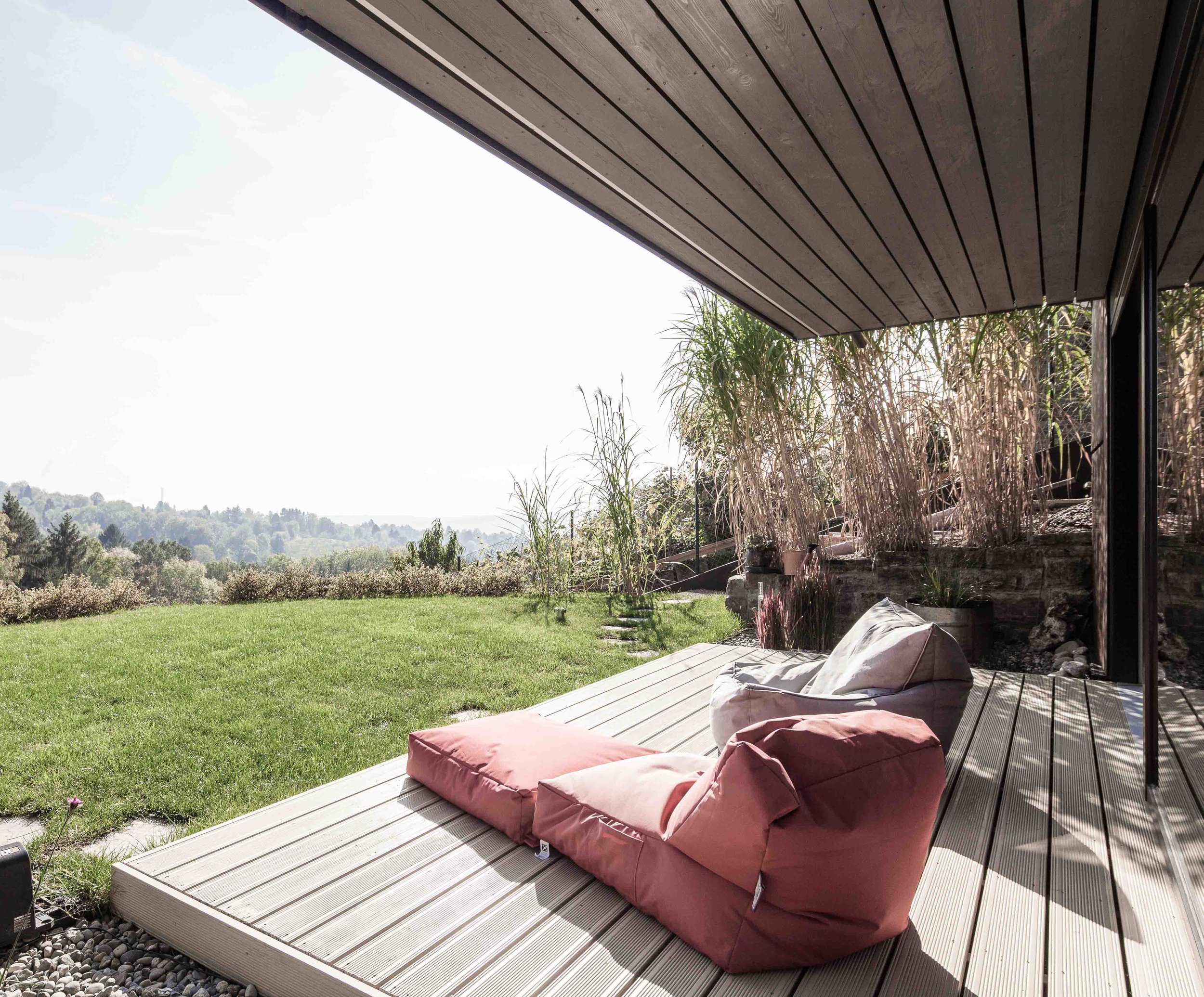 haus GRO - Blick auf eine Veranda mit Sitzkissen und Blick auf eine grüne Wiese und Bäume.
