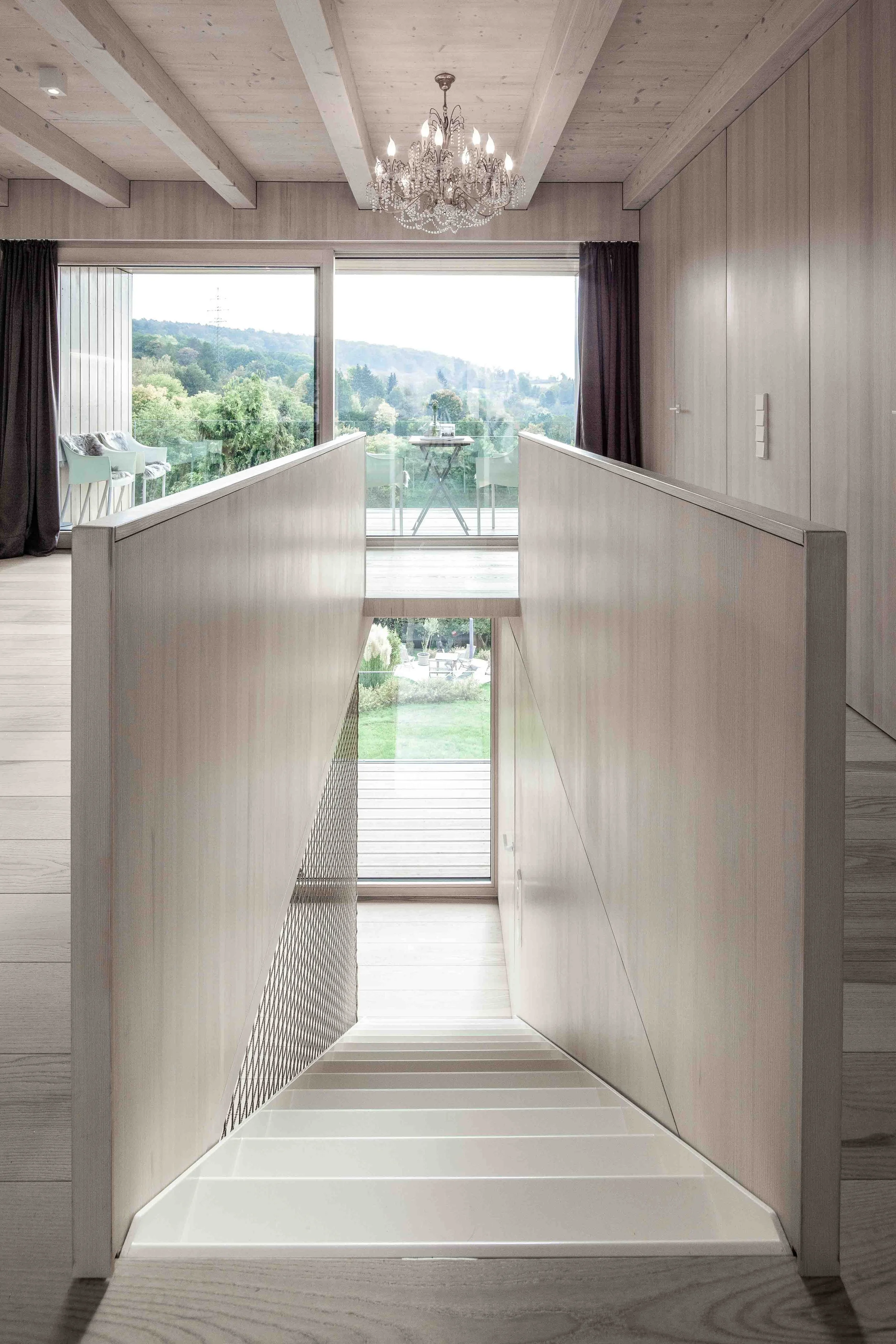 haus GRO - Innenraum eines Hauses mit Holzdecken, großer Fensterfront, balkon, und Blick ins Grüne bei Tageslicht.