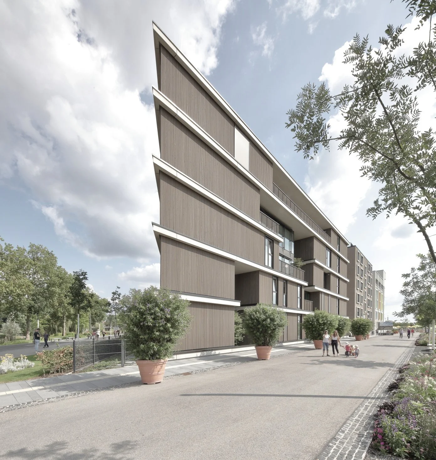 kinderhaus BUGA - Modernes Mehrfamilienwohnhaus mit mehreren Stockwerken, große Fenster und Balkone, umgeben von Bäumen und Blumen, Spaziergänger im Vordergrund, sonniger Tag mit Wolken am Himmel.