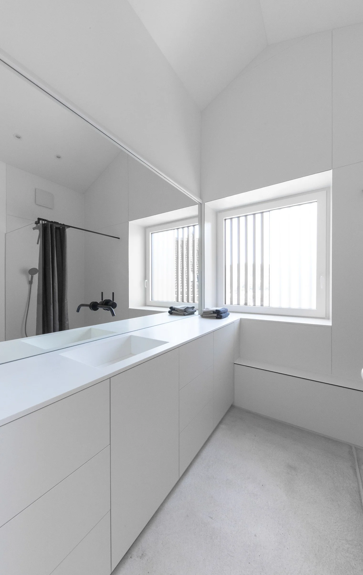 haus RU - Modernes Badezimmer mit weißer Oberfläche, Doppelwaschbecken, großer Fenster mit Jalousien, dunklen Handtüchern und Regenschauer-Duschkopf