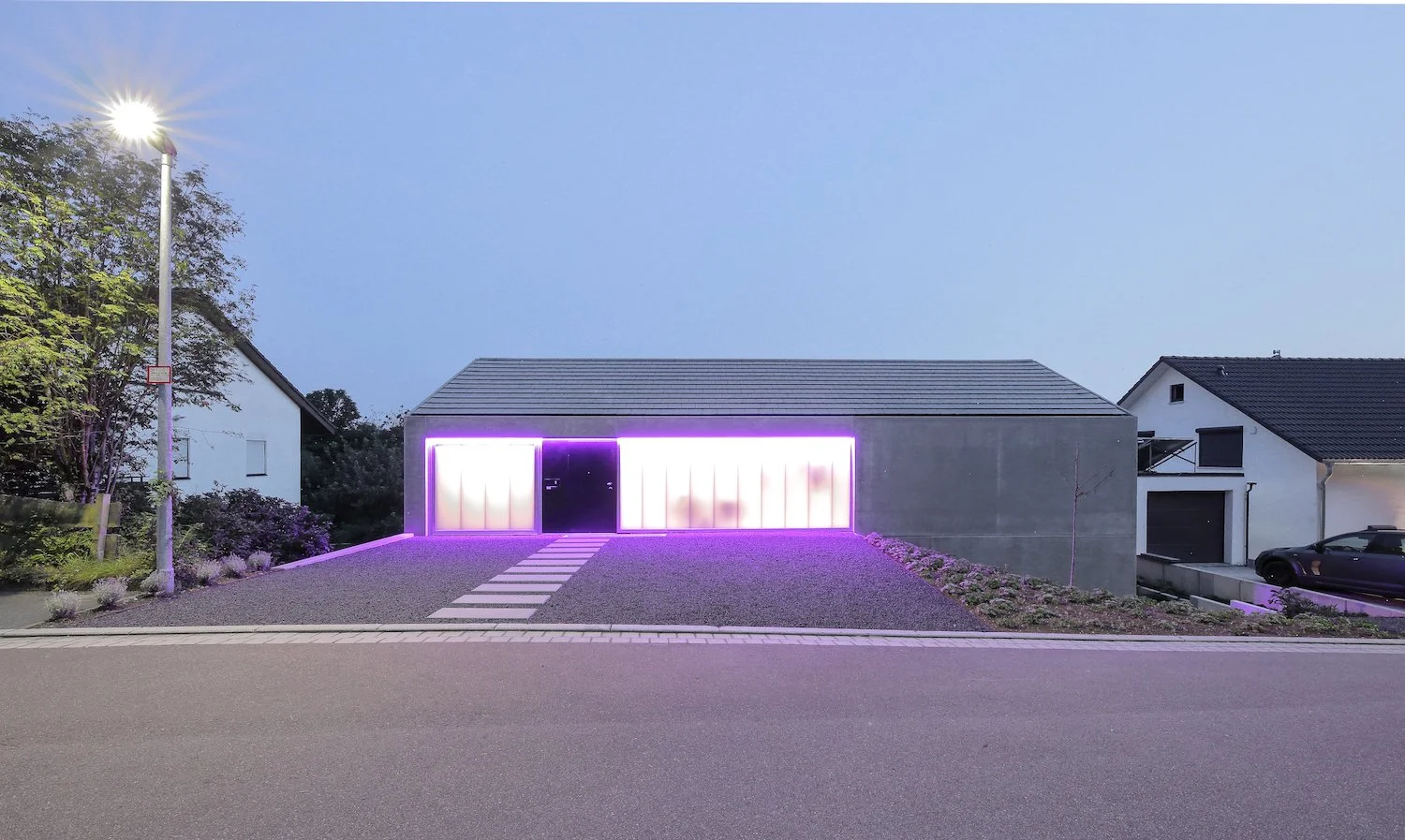 haus WÄ - Modernes Haus mit LED-Beleuchtung im Eingangsbereich bei Dämmerung, Straße davor.
