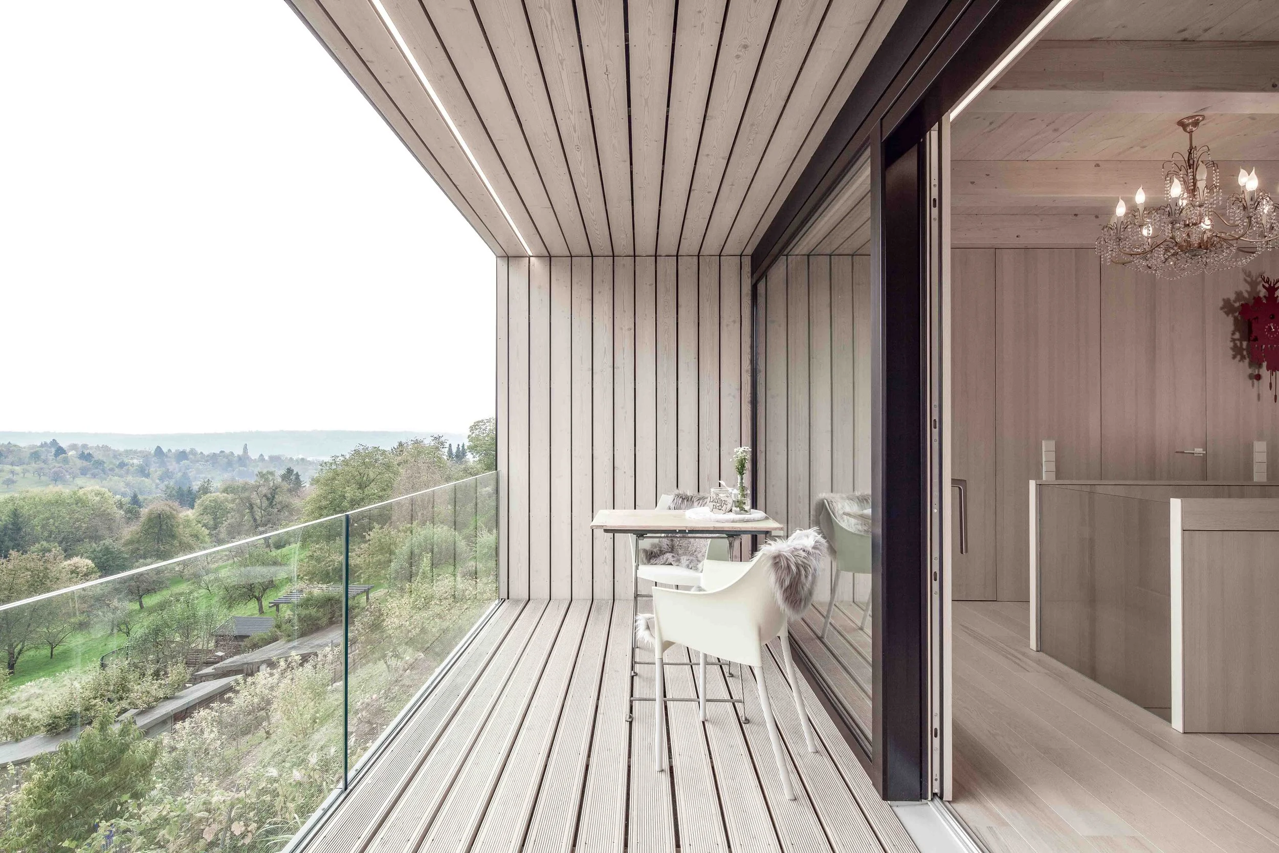haus GRO - Ein moderner Balkon mit Holzverkleidung und Glasgeländer bietet einen Blick auf eine grüne Landschaft mit Bäumen und Feldern.