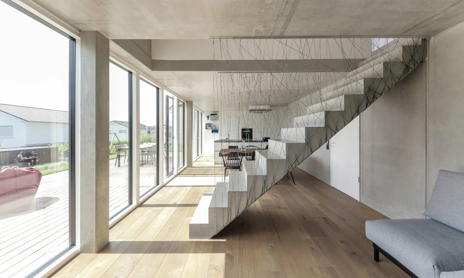 haus WÄ - Innenansicht eines modernen Hauses mit großen Glasfenstern, Holzfußboden, offener Grundriss und sichtbarer Betondecke.