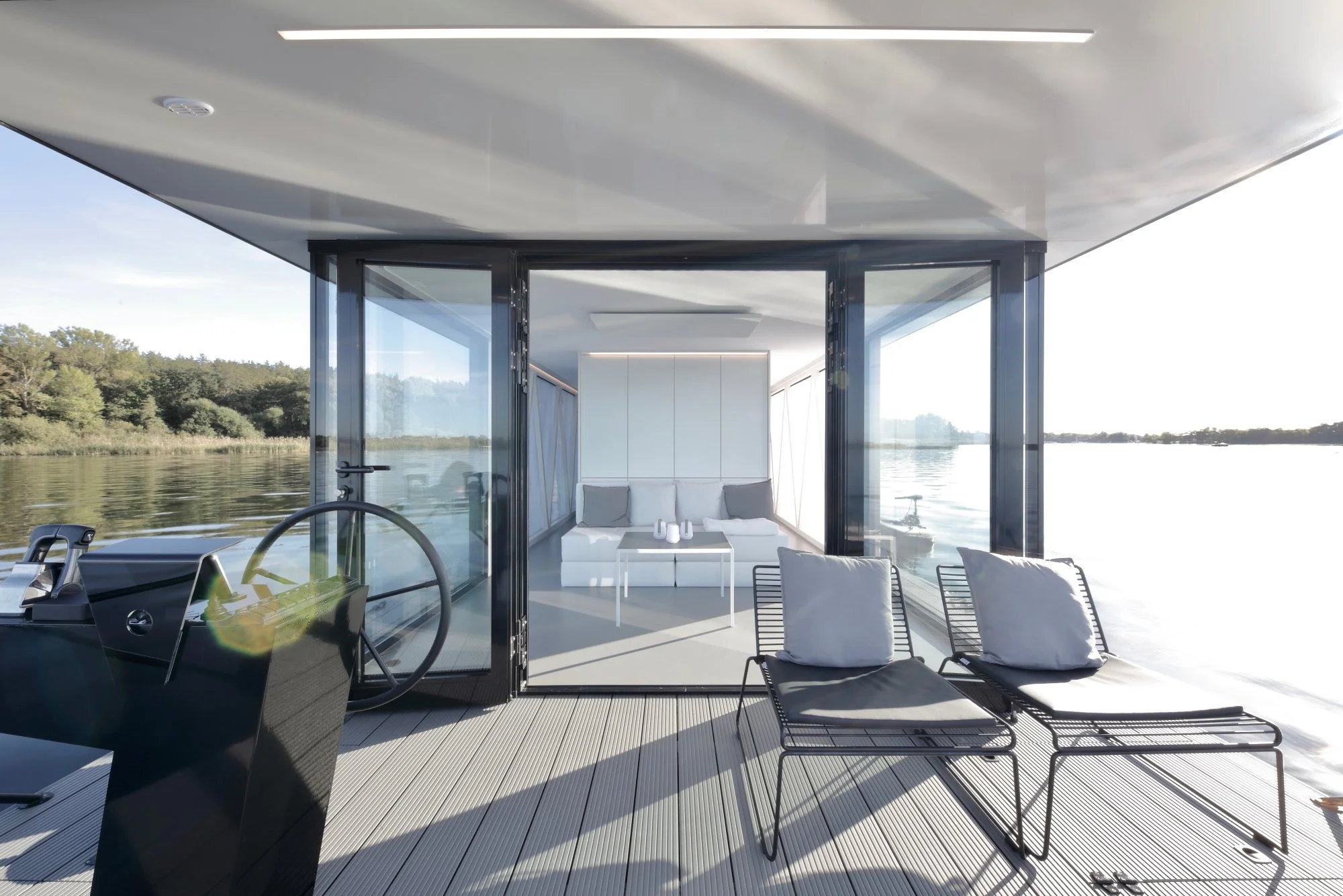 Ein moderner Hausboot-Innenraum mit Blick auf den Fluss, Sonnenliegen und einem weißen Sofa