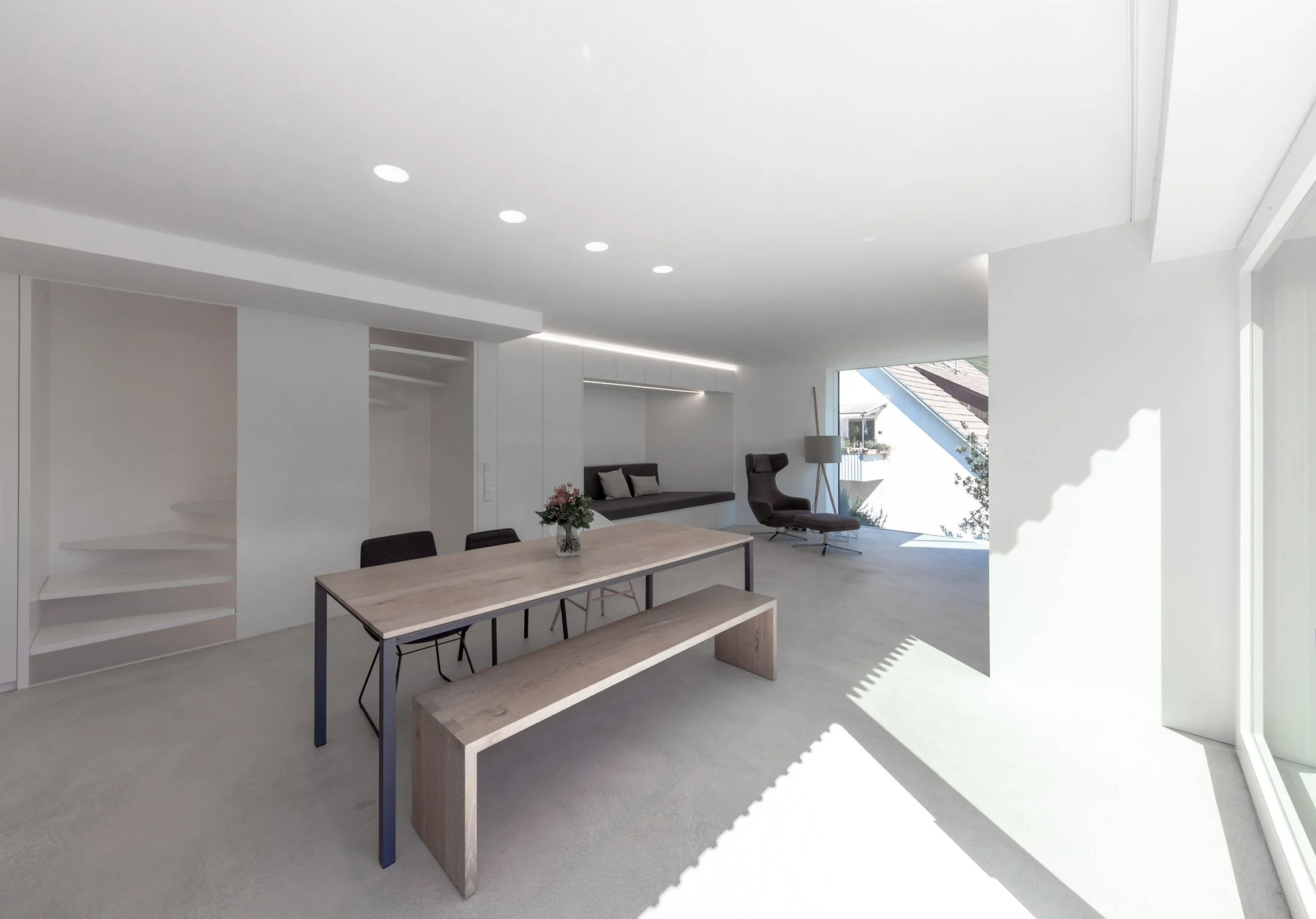 haus RU - Modernes, helles Wohnzimmer mit großen Fenstern, minimalistische Möbel, Esstisch, ein Sessel, und eine Lampe.