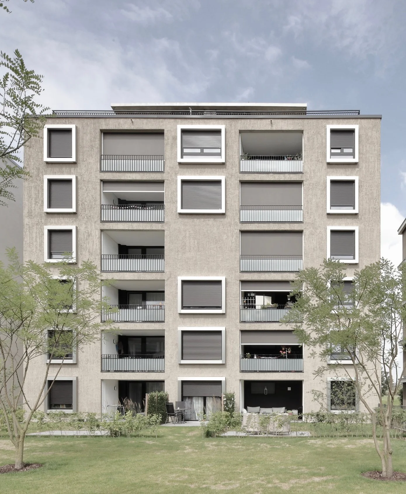 wohnhaus BUGA - Mehrstöckiges modernes Wohngebäude mit Balkonen und geschlossenen Rollos, umgeben von Bäumen und einem Grünbereich im Vordergrund.