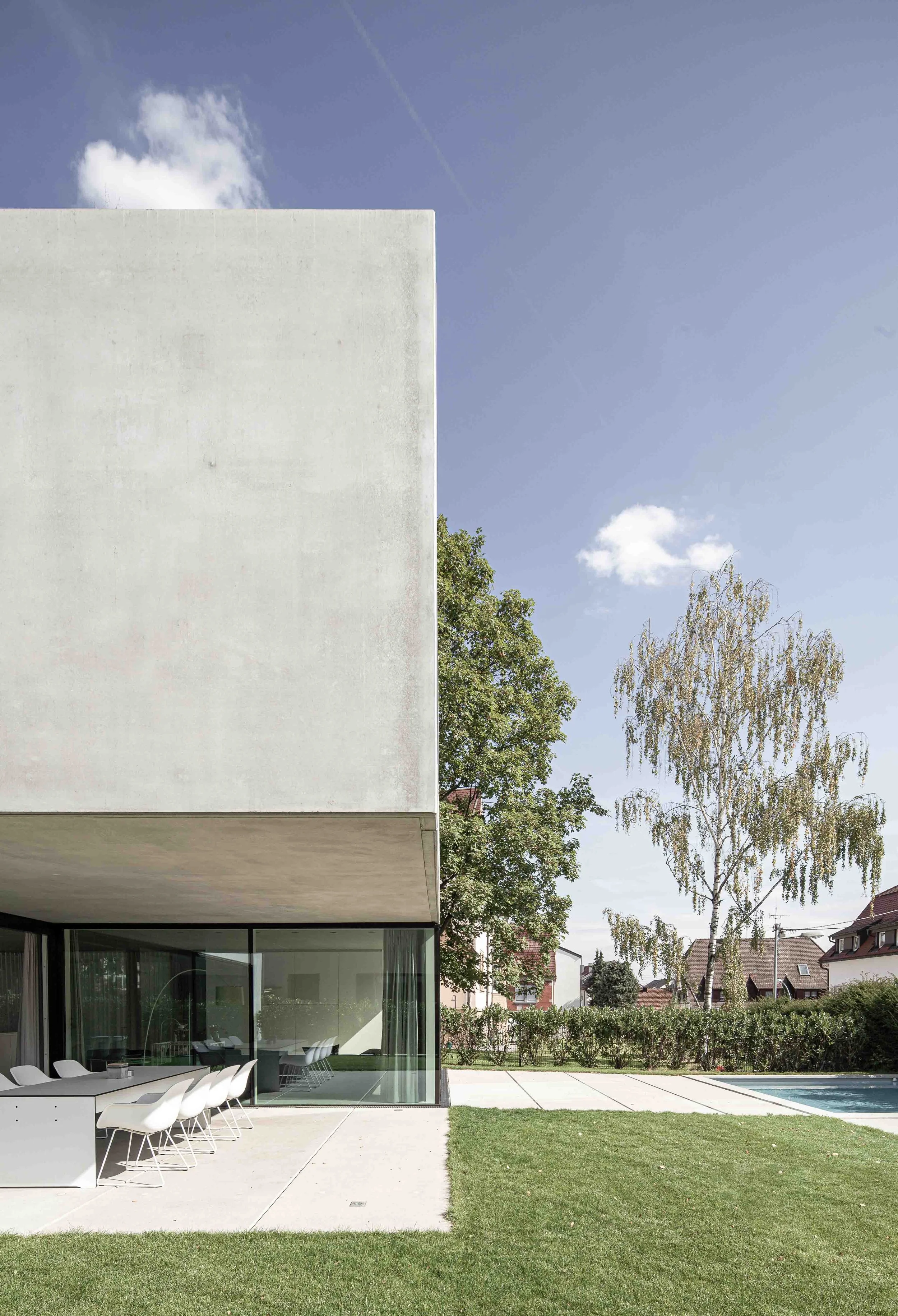 haus vO - Ein modernes Haus mit einer großen Fensterfassade, einem Garten mit Rasen, einem Pool und einem Esstisch mit weißen Stühlen im Außenbereich.