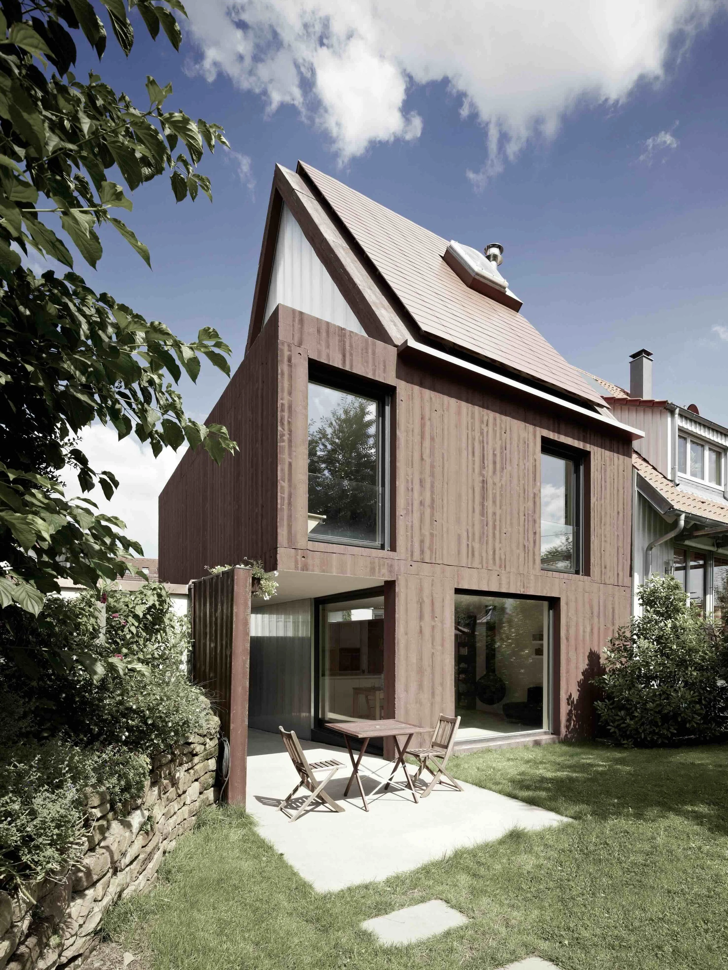 haus - B_Modernes Einfamilienhaus mit Holzfassade, steilem Dach und Terrasse mit Gartenmöbeln bei sonnigem Wetter