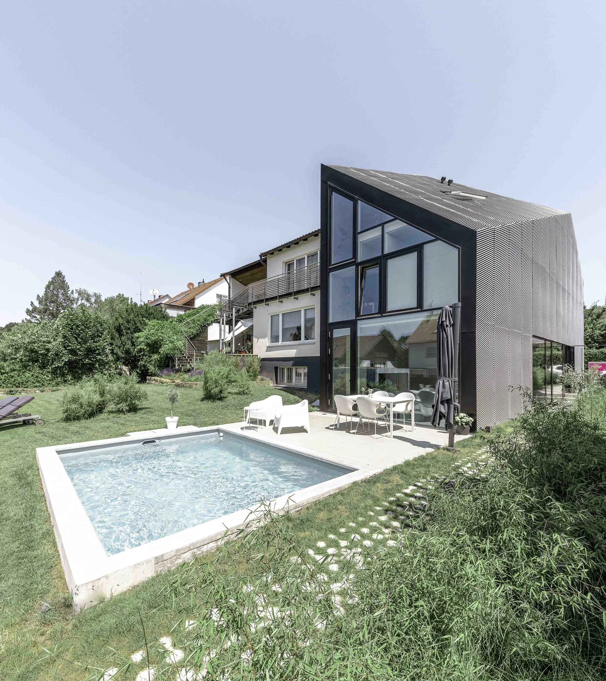 Garten mit einem kleinen Pool, modernen Möbeln und einem modernen Gebäude im Hintergrund.
