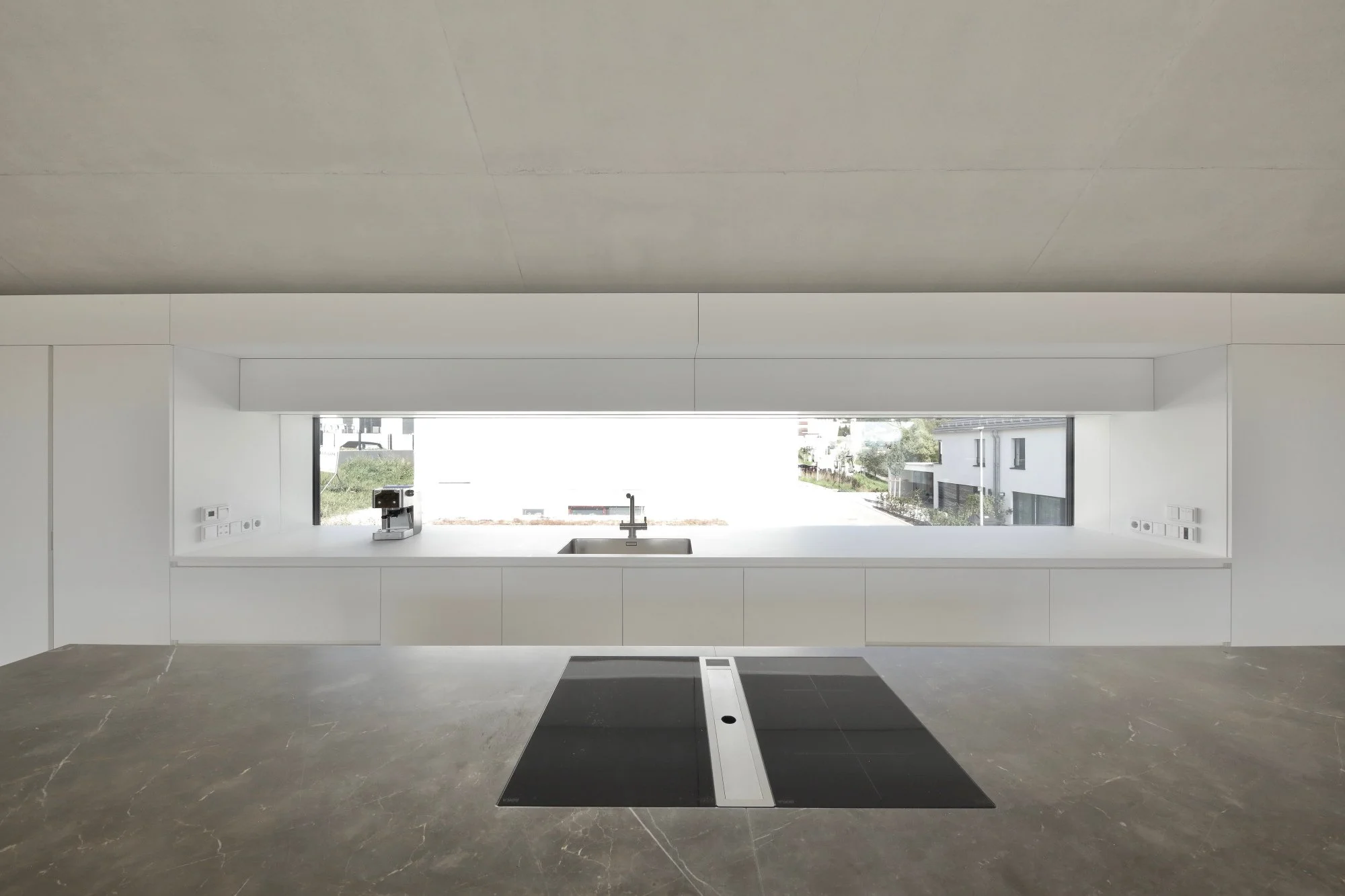 haus CC - Moderne, minimalistische Küche mit großem Fenster, Waschbecken, schwarzen Kochflächen und weißen Unterschränken.