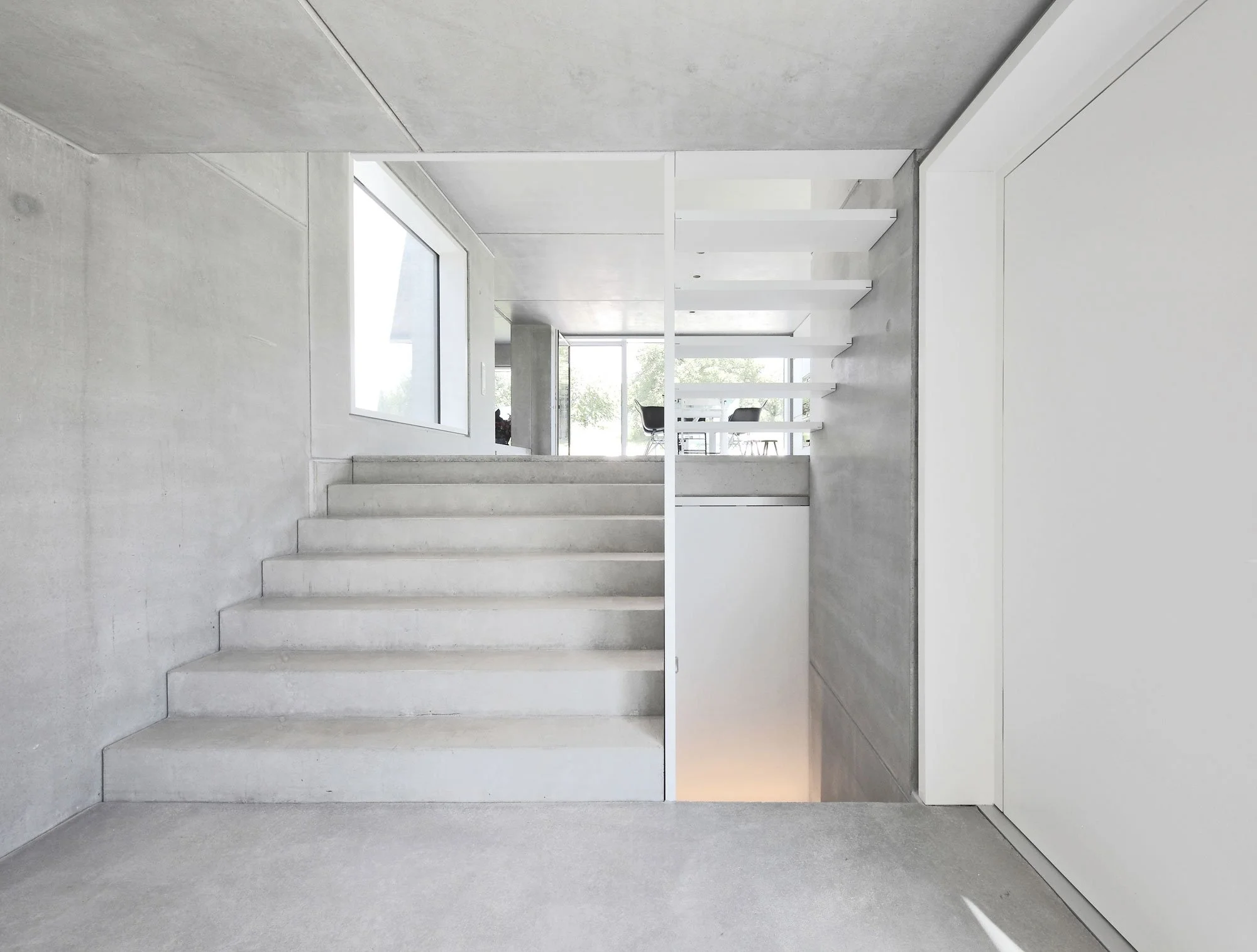 haus SG - Innenansicht eines modernen, minimalistischen Hauses mit weißen Wänden, Treppenaufgang, großen Fenstern und viel natürlichem Licht.