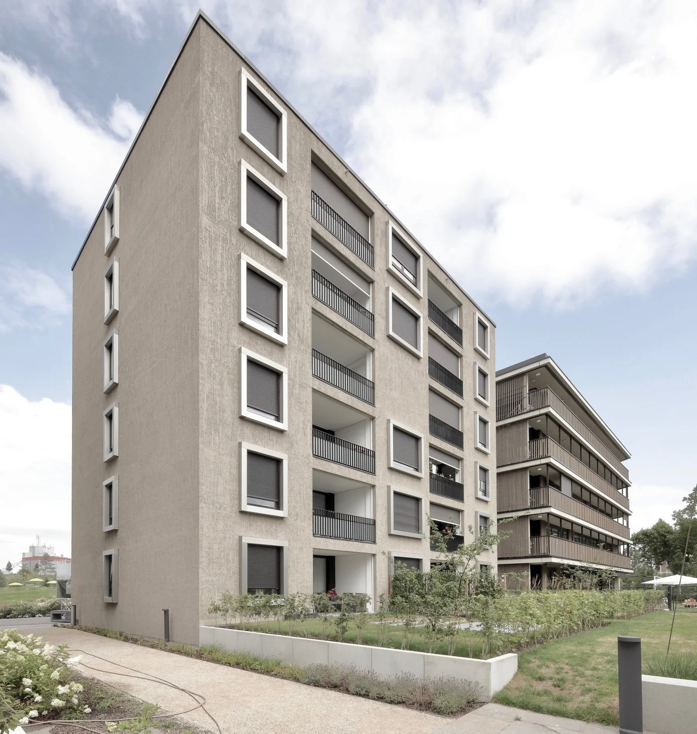 wohnhaus BUGA - Zwei moderne Mehrfamilienhäuser mit Balkonen, eine Grünanlage mit Bäumen und Blumen im Vordergrund, bei bewölktem Himmel.