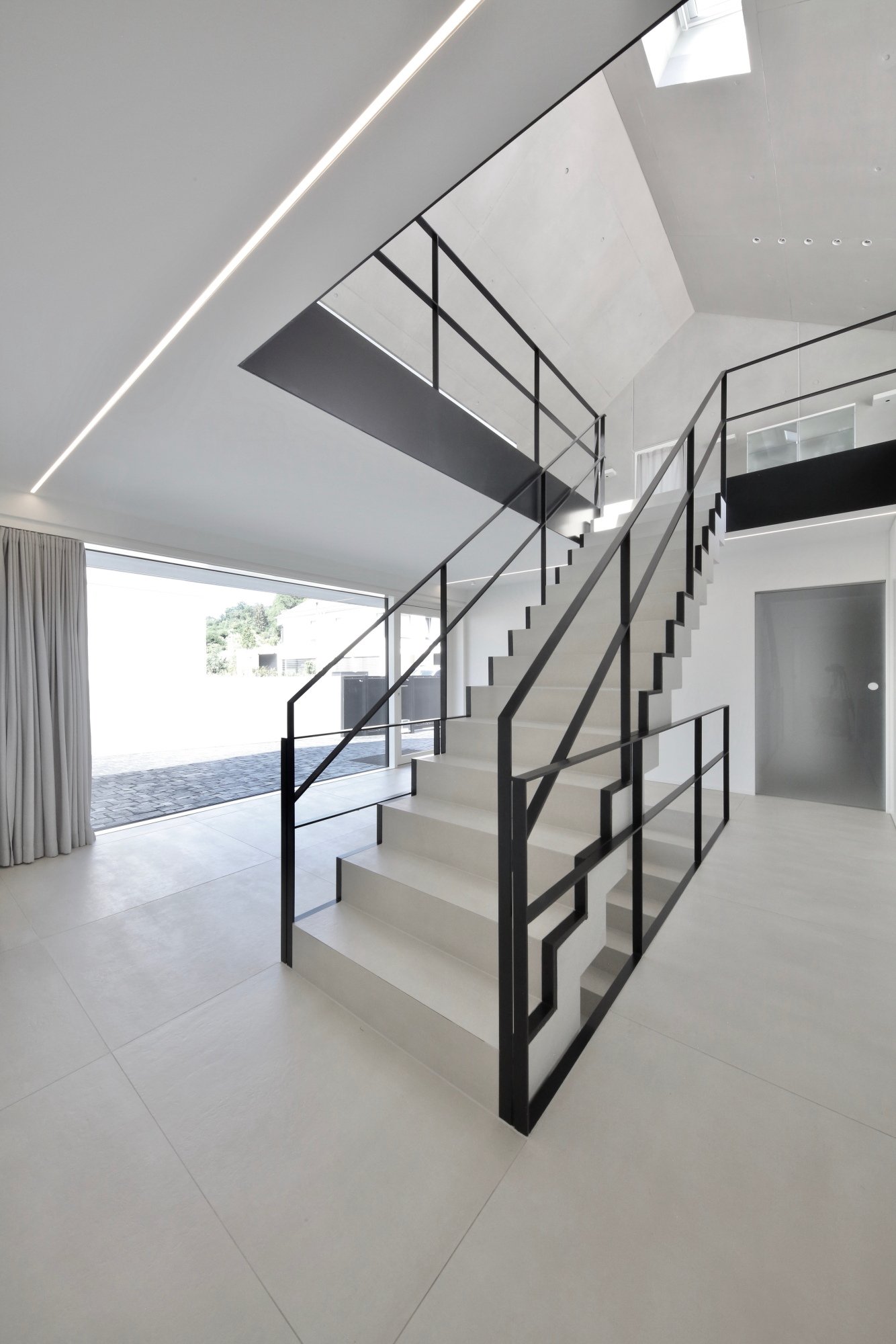  haus CC - moderner Treppenaufgang in einem hellen, minimalistischen Haus, mit schwarzem Geländer, großem Fenster und weißen Fließen