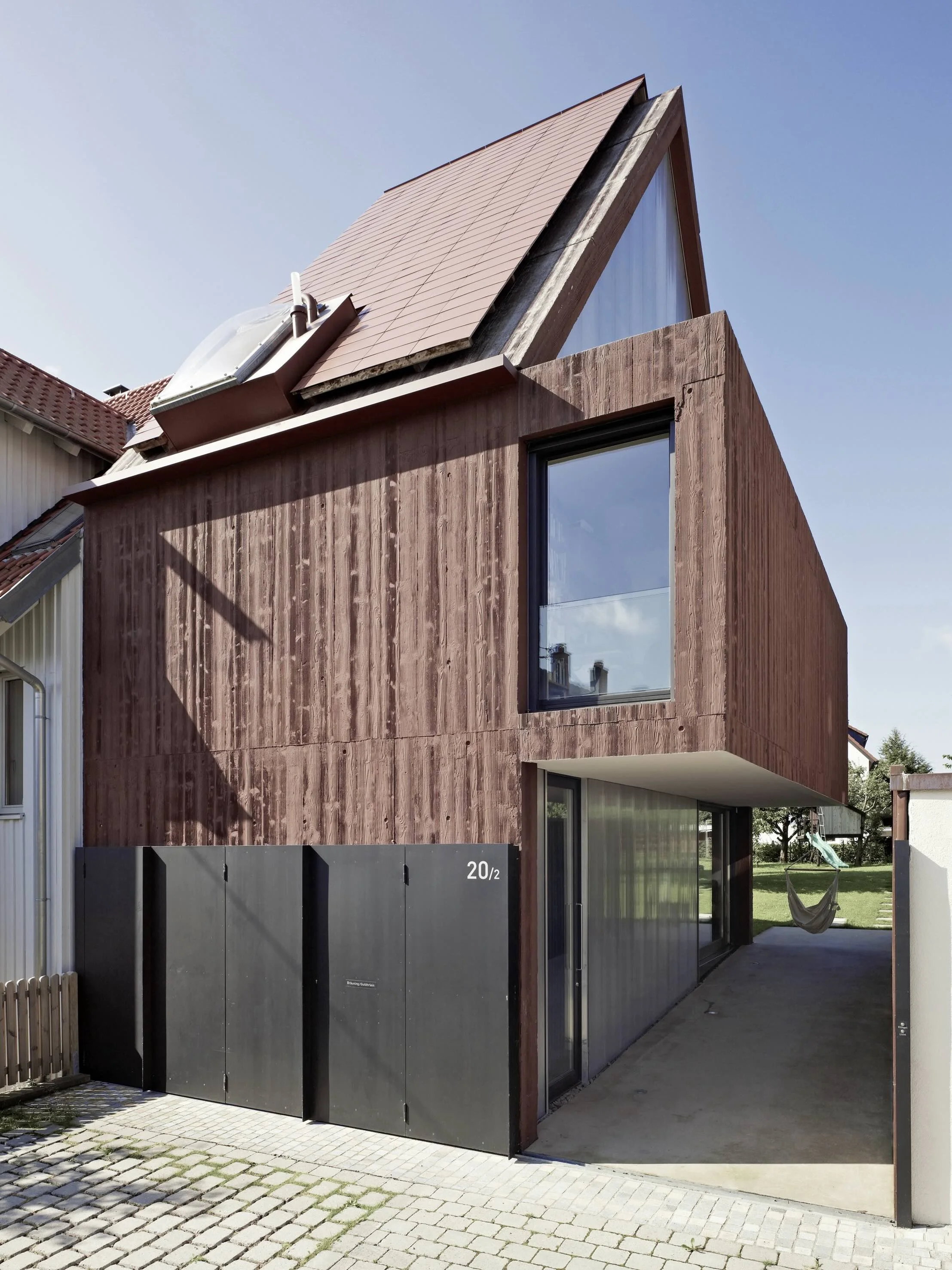 haus - B_Modernes Wohnhaus mit markantem Satteldach, Holzfassade, großen Fenstern und überdachtem Eingangsbereich an einem sonnigen Tag