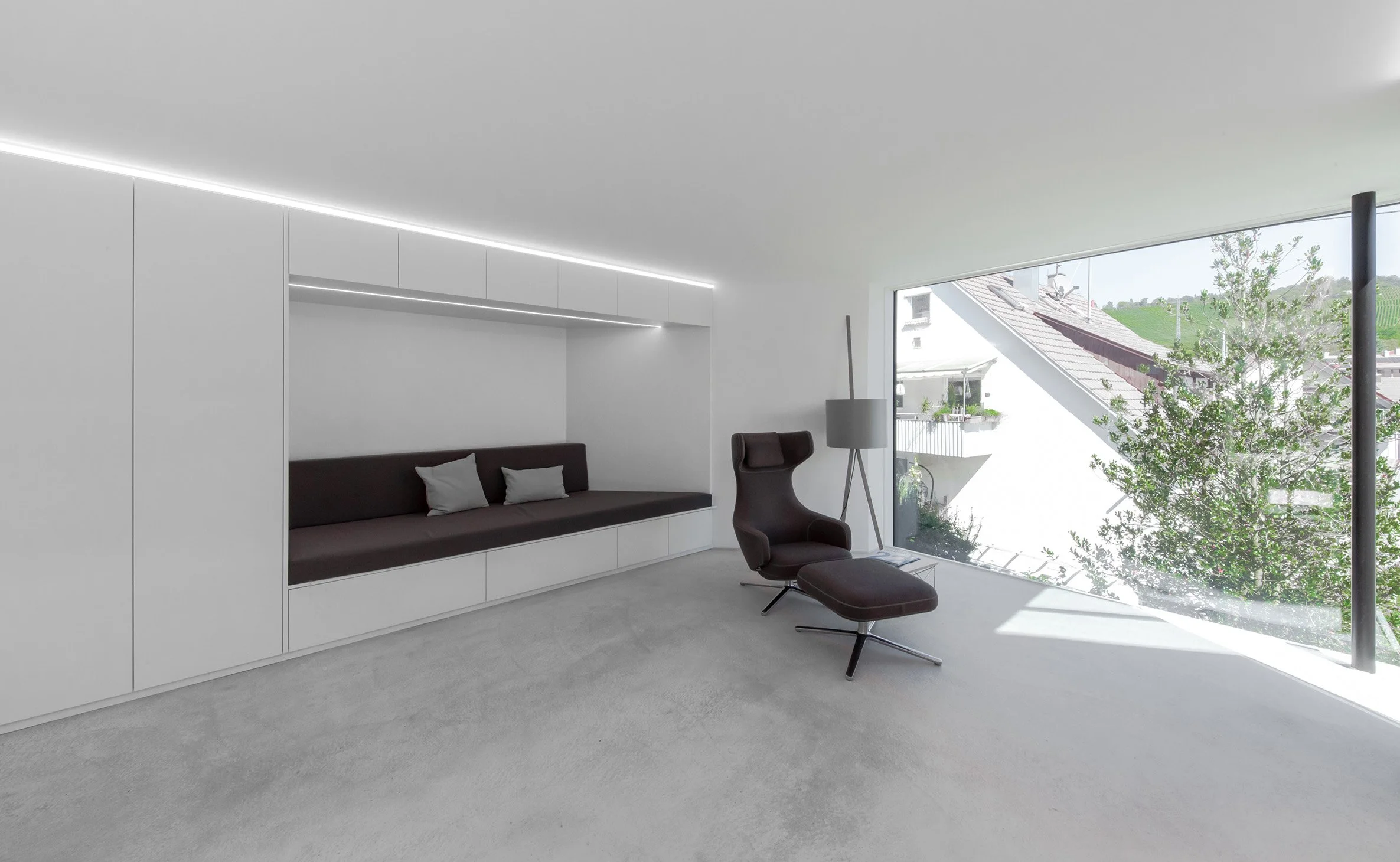haus RU - Modernes, minimalistisch eingerichtetes Wohnzimmer mit großen Fenstern, einem schwarzen Sessel, einem Hängesofa mit Kissen, einer Stehlampe und einer weißen Wand mit eingebauten Schränken.