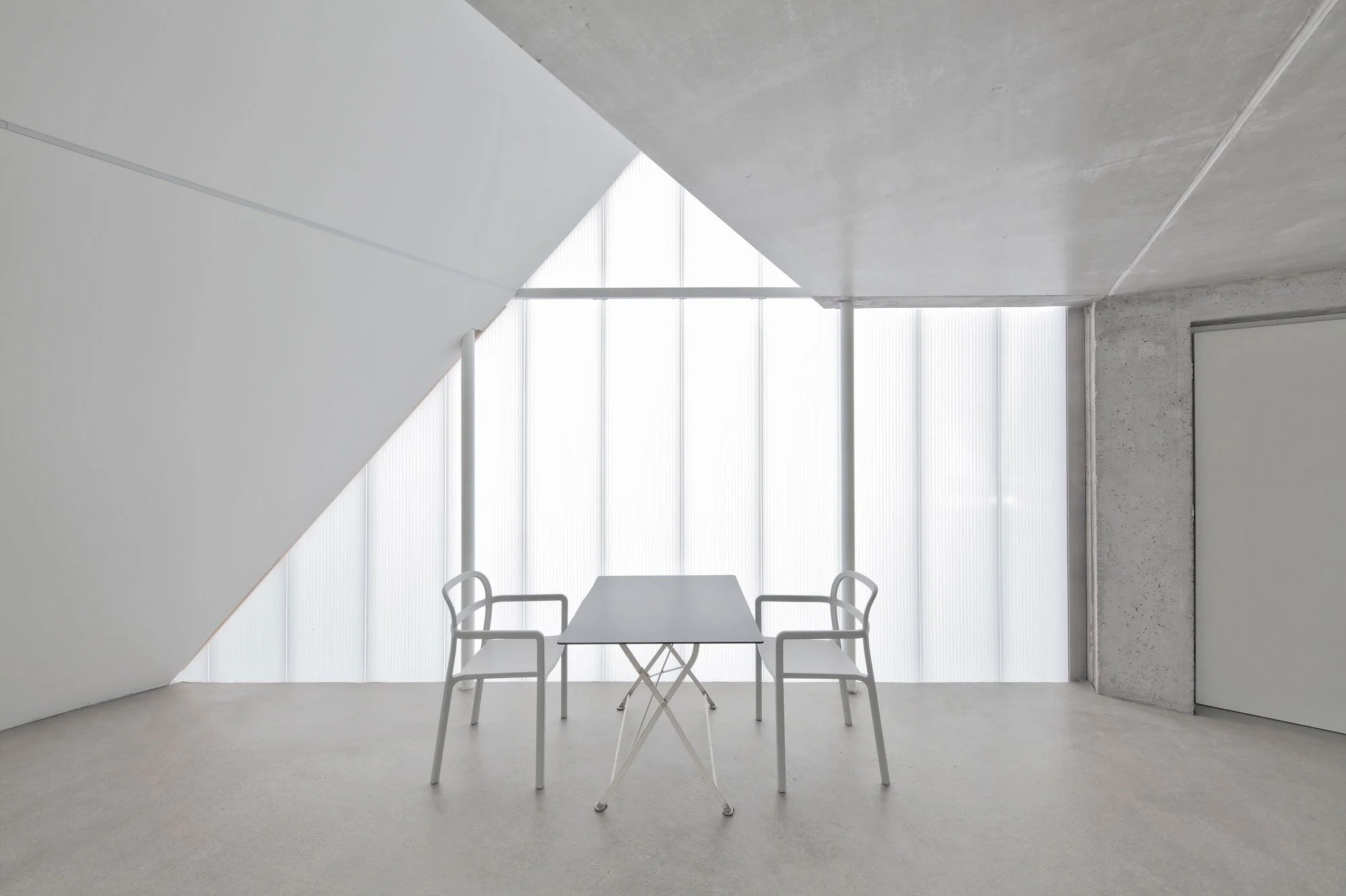 haus SO - Ein heller, minimalistischer Raum mit weißen Wänden, großen Fenstern und drei weißen Stühlen um einen Tisch.