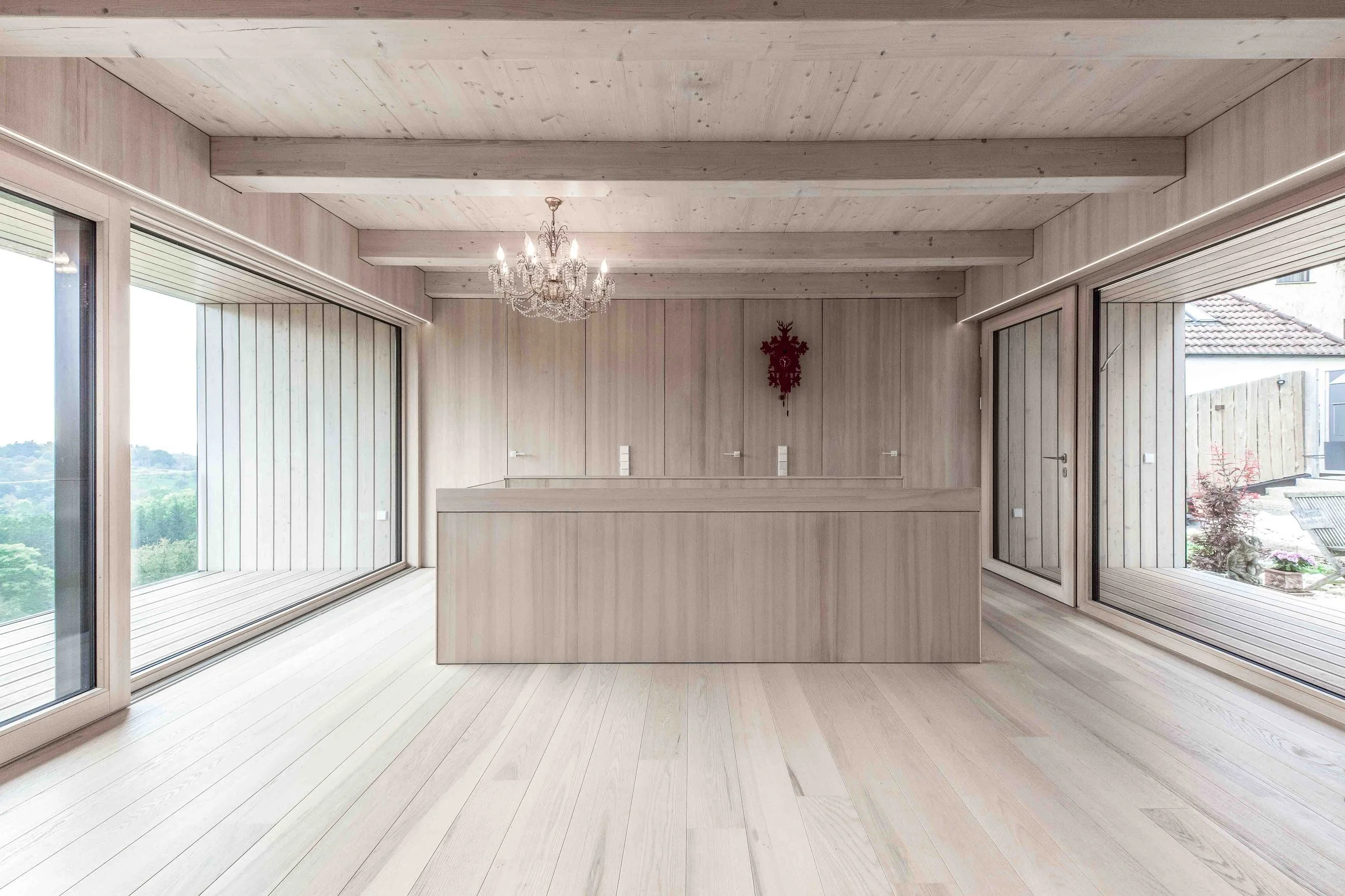 haus GRO - Innenraum eines modernen, hellen Hauses mit viel Holz, große Fenster und eine Kronleuchter an der Decke.