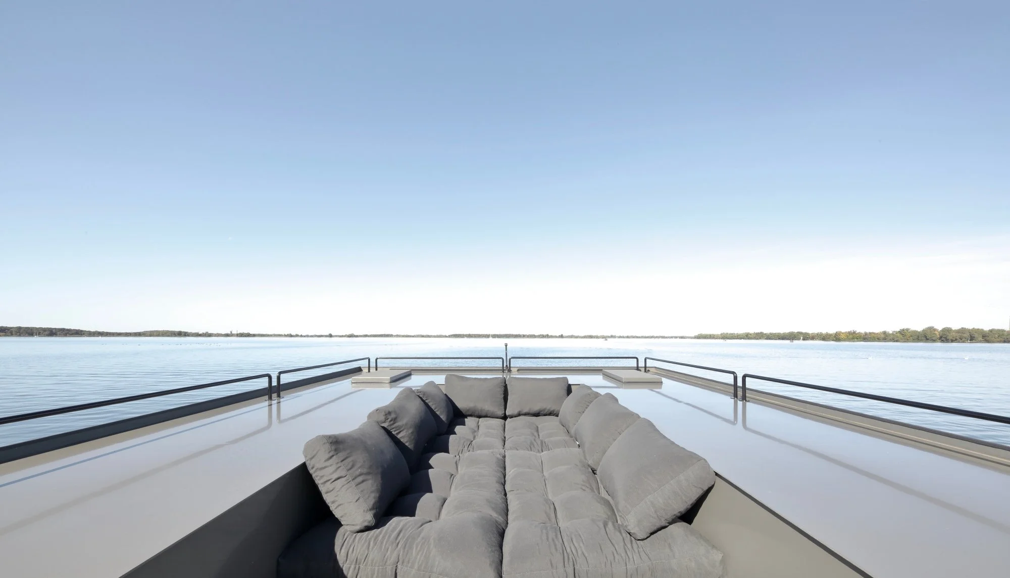 Liegefläche mit grauen Kissen auf einem offenen Boot mit Blick auf den ruhigen See und den Himmel.