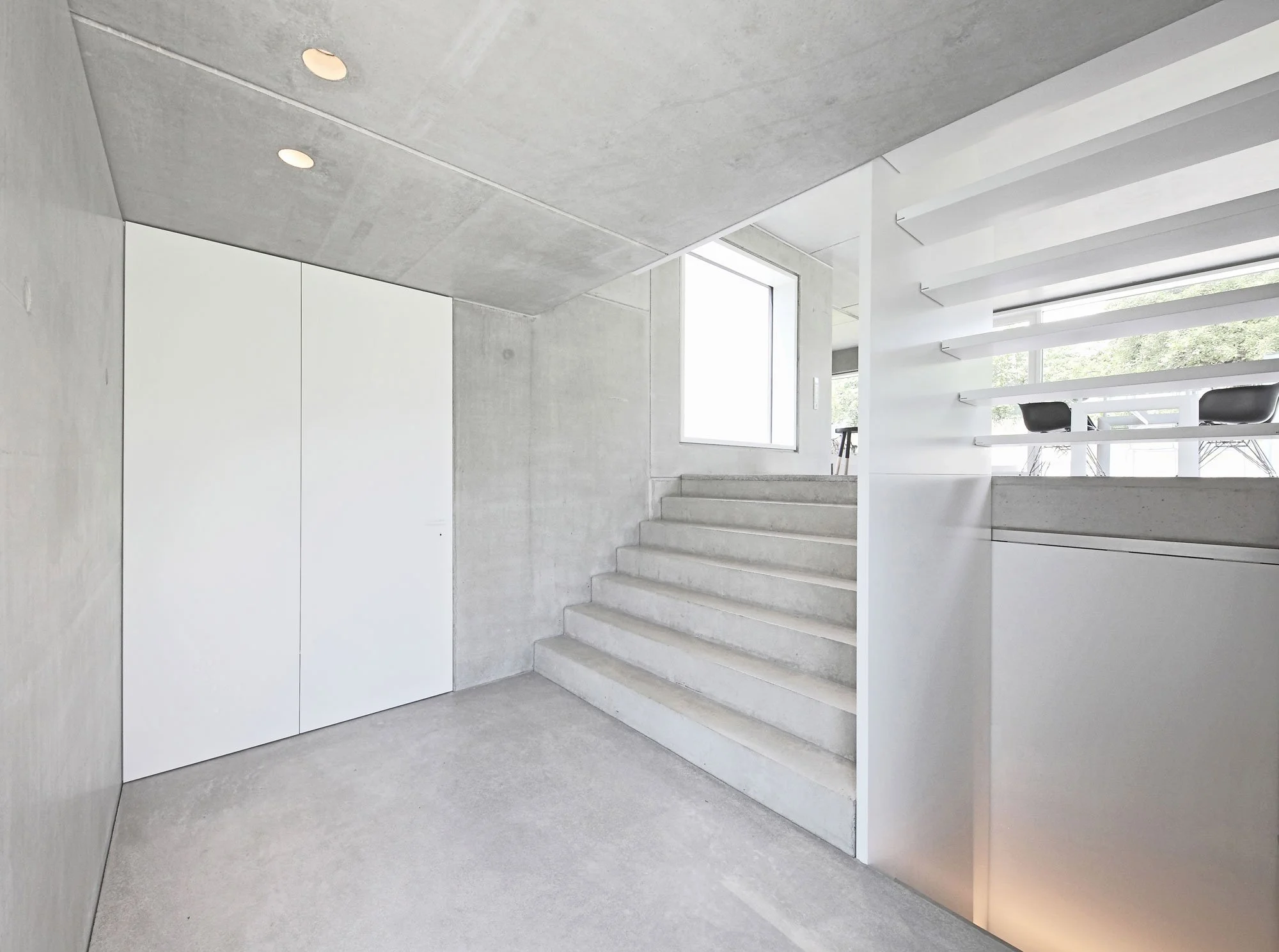 haus SG - Ein moderner, minimalistischer Eingangsbereich mit Betontreppe, weißen Wänden, großen Fenstern und stilvoller Beleuchtung.