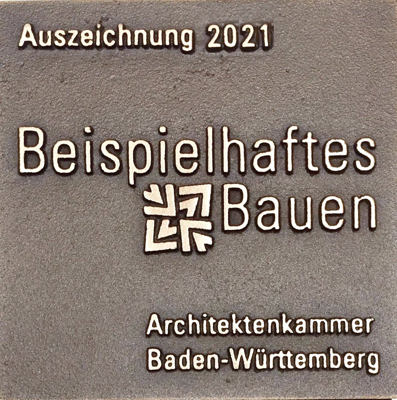 'Auszeichnung 2021 Beispielhaffes Bauen Architektenkammer Baden-Württemberg' und einem Symbol aus mehreren überlappenden Pfeilen in der Mitte.