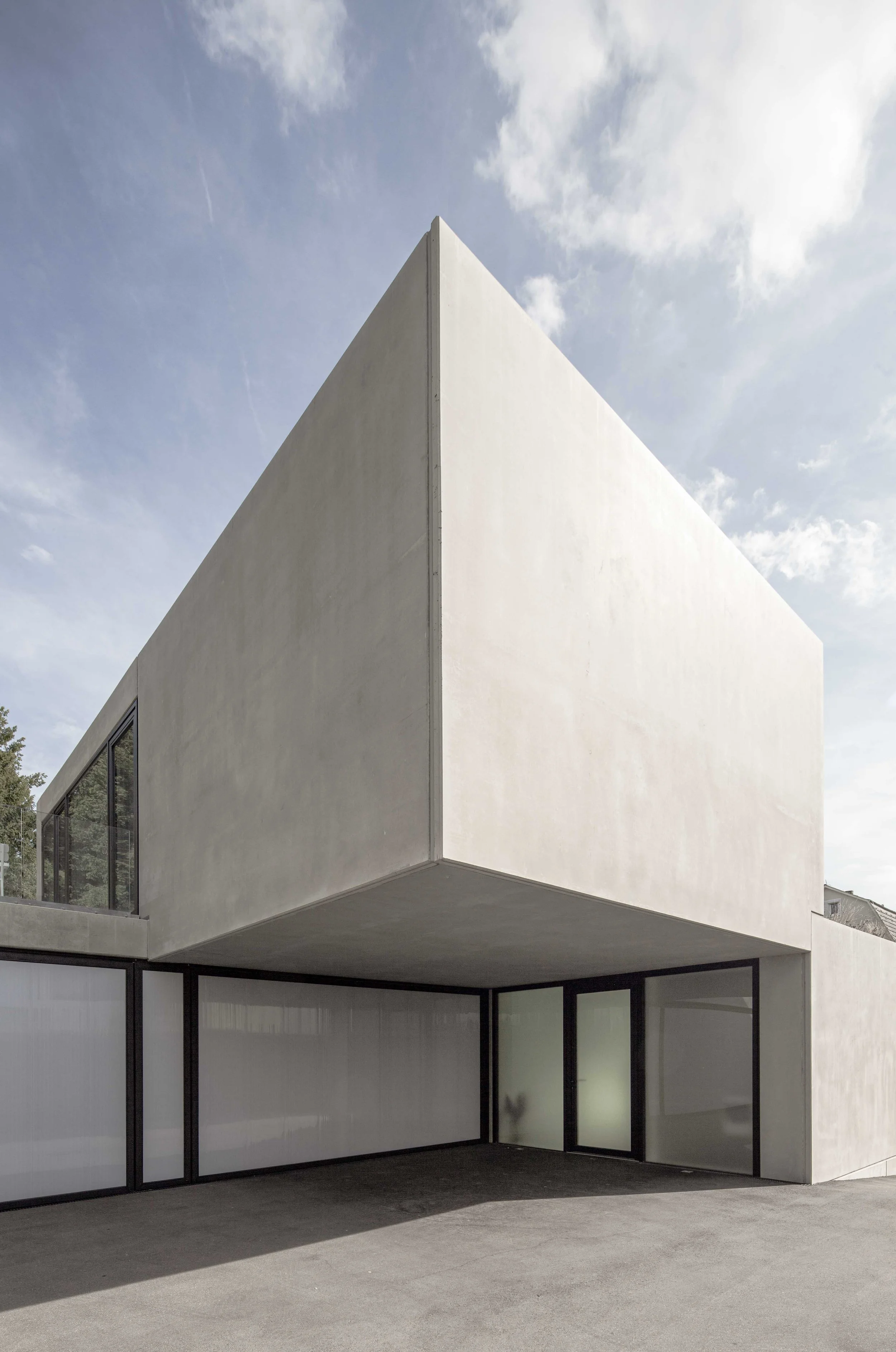 haus vO - Modernes weißes Gebäude mit großen Fenstern und Balkon, gegen Himmel mit Wolken.