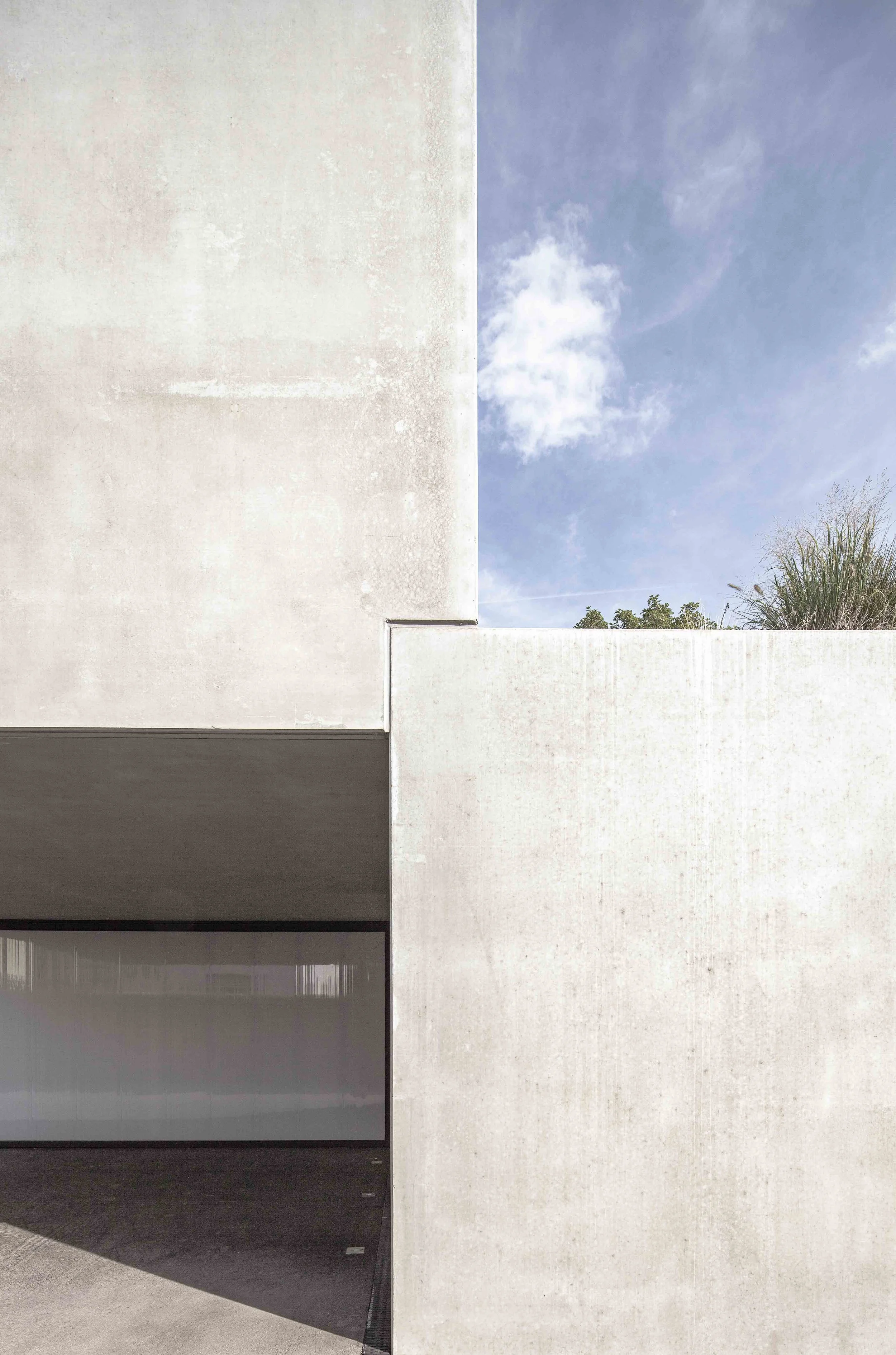 haus vO - Ein modernes Gebäude mit weißen Wänden, ein offener Eingang und ein blauer Himmel im Hintergrund, teilweise mit Wolken und einigen Büschen.