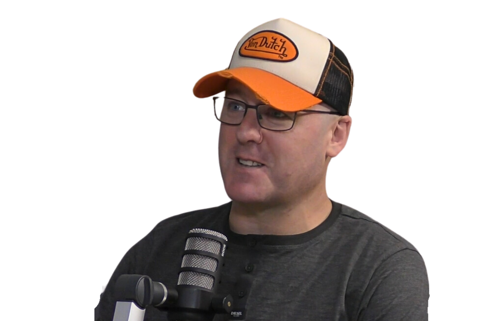 A man wearing glasses and a black and orange trucker hat with the logo 'Von Dutch' is speaking into a podcast microphone.