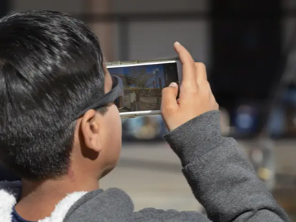 A person with short dark hair and glasses taking a photo with a smartphone.