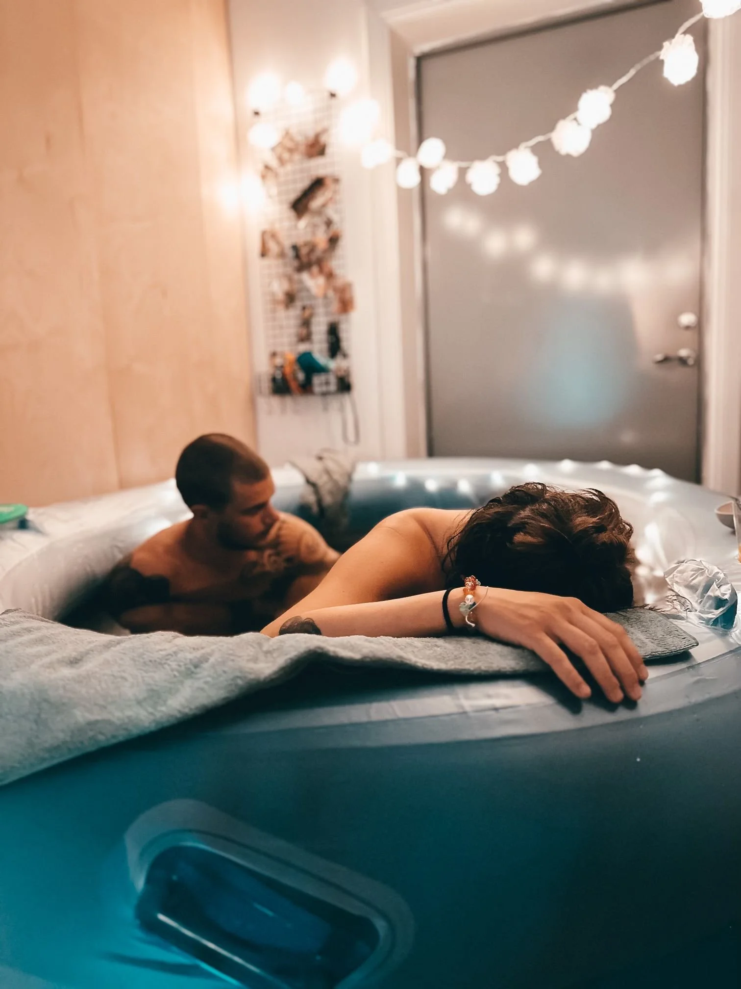 People relaxing in a hot tub, with a cozy indoor setting decorated with string lights and a photo board on the wall.