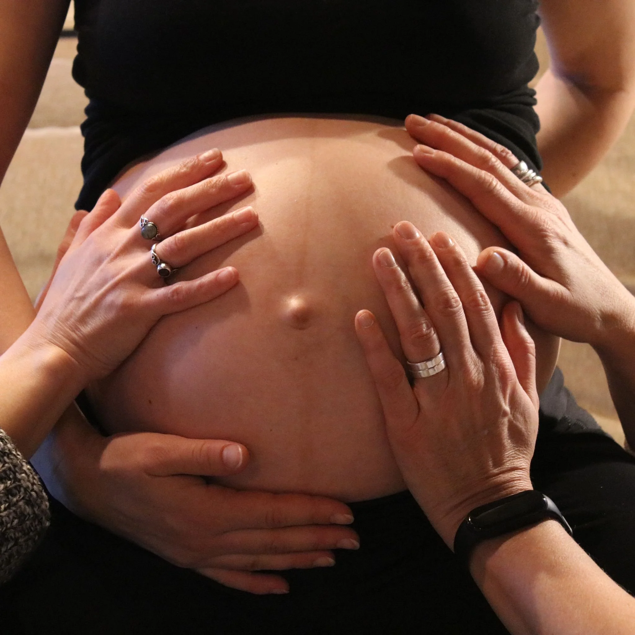 Hands placed on a person's stomach, with rings on fingers, touching the skin.