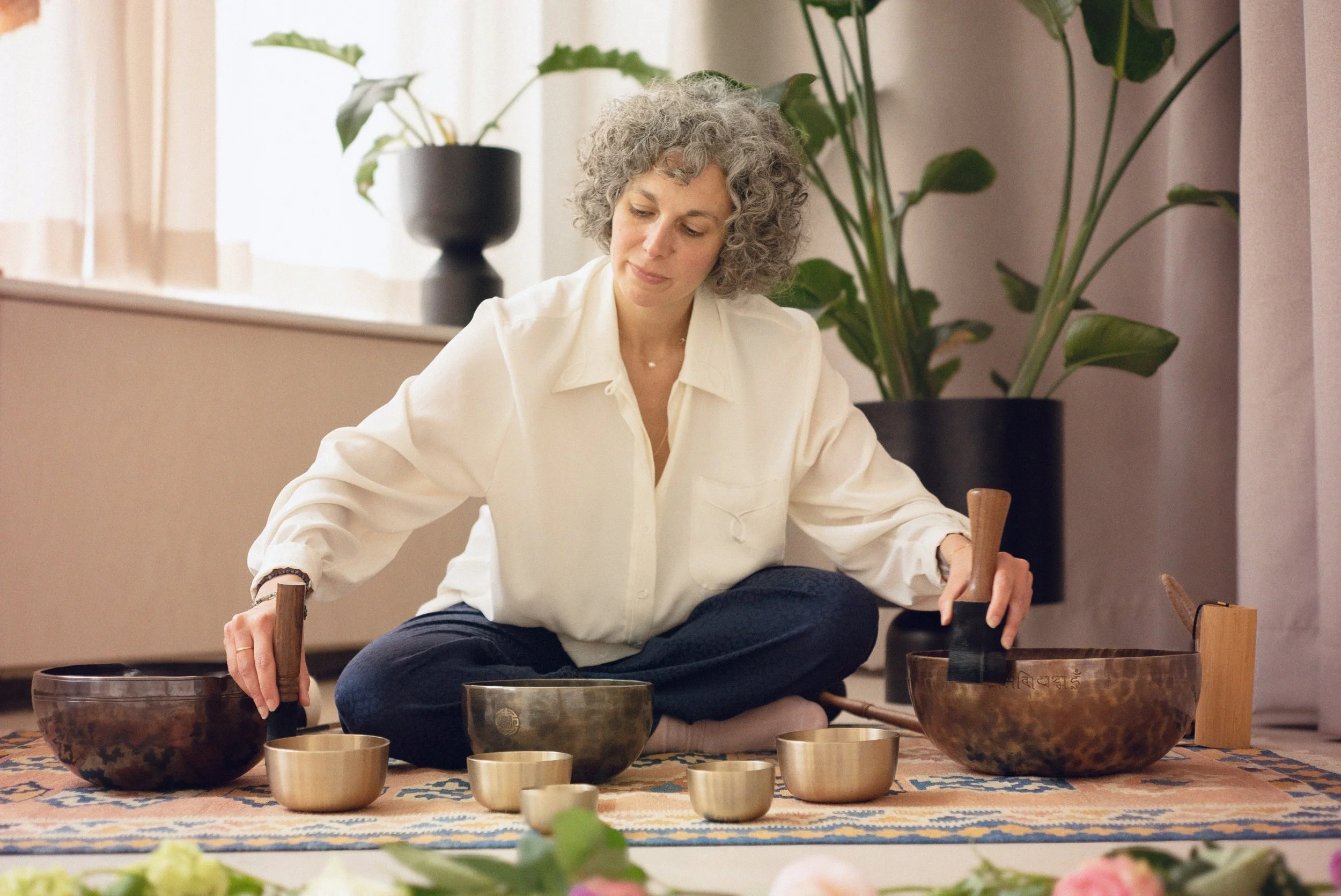 Woman sitting cross-legged and playing singing bowls during a sound meditation session