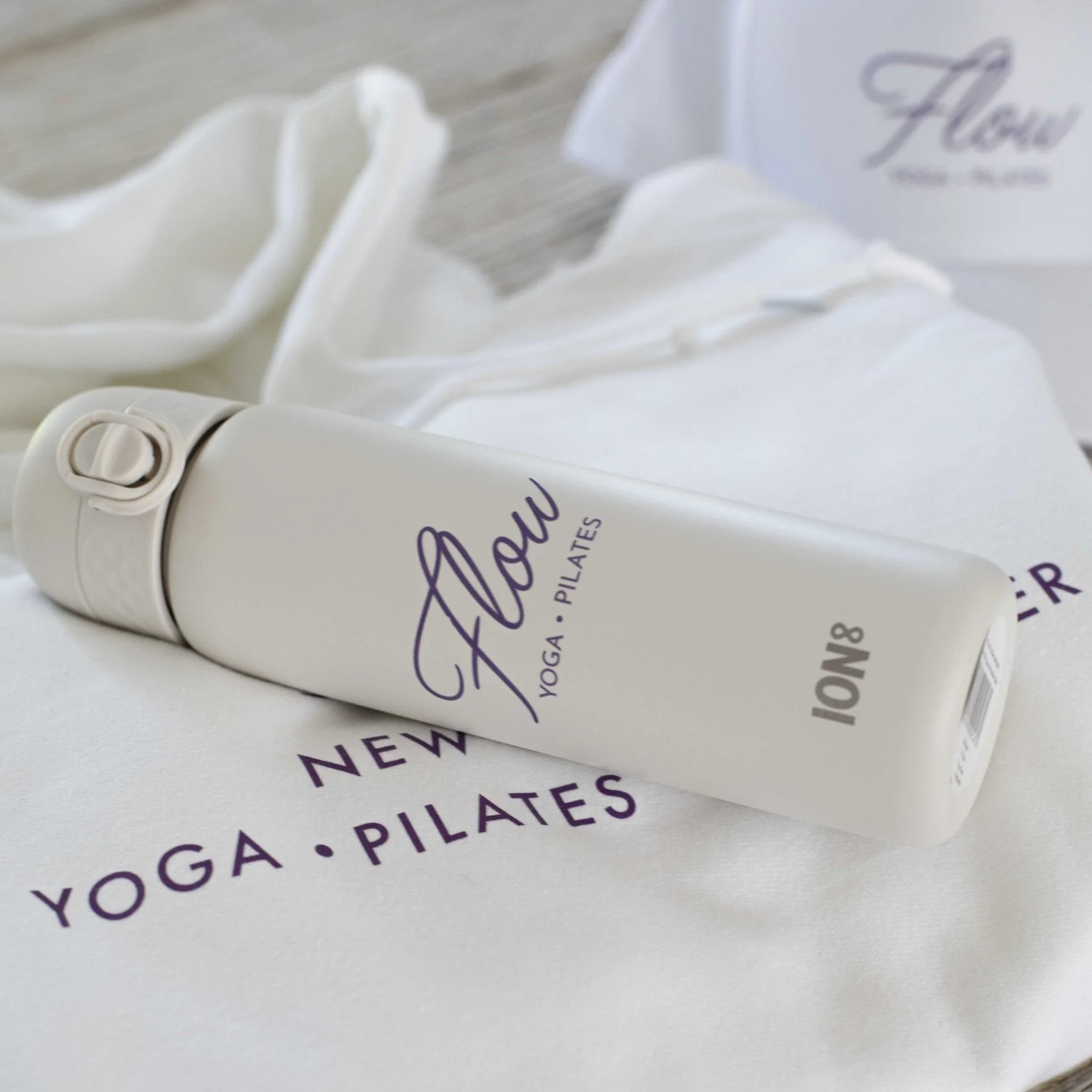 Close-up of a white tube labeled 'Glow' with purple text, lying on a white surface, with a white paper or box behind it with similar purple text.