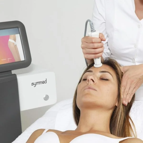 A woman receiving an ultrasound treatment on her forehead in a clinical setting, with a medical device nearby.