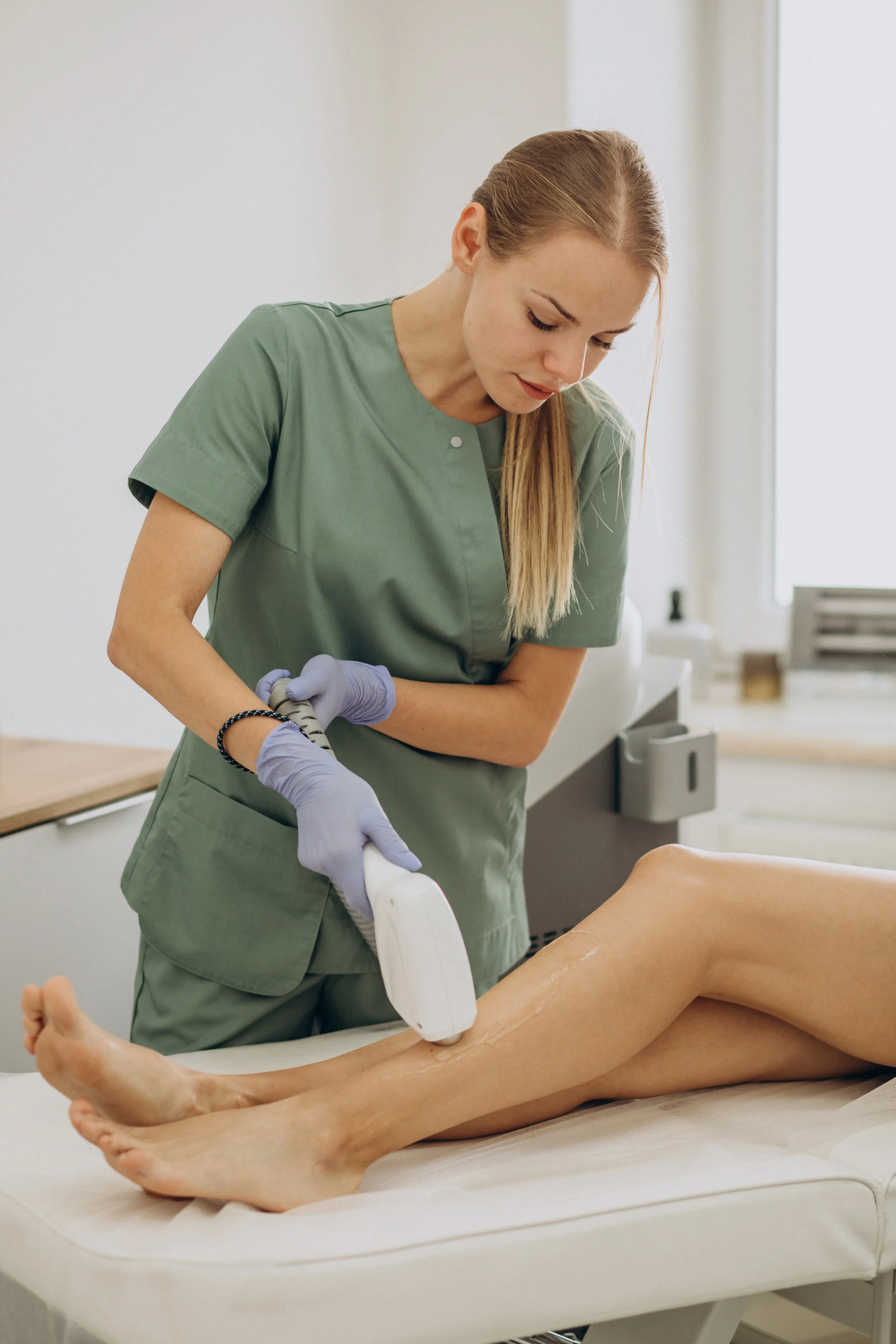 A medical professional performs laser hair removal on a patient's leg in a clinical setting.