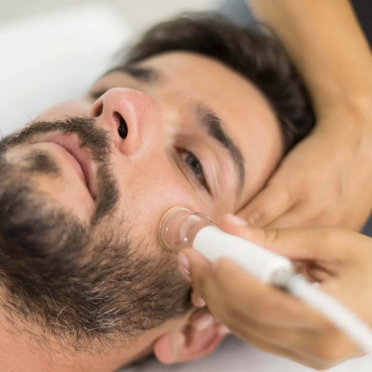 A man receiving a facial treatment, with a skincare product applied to his cheek using a cotton pad.