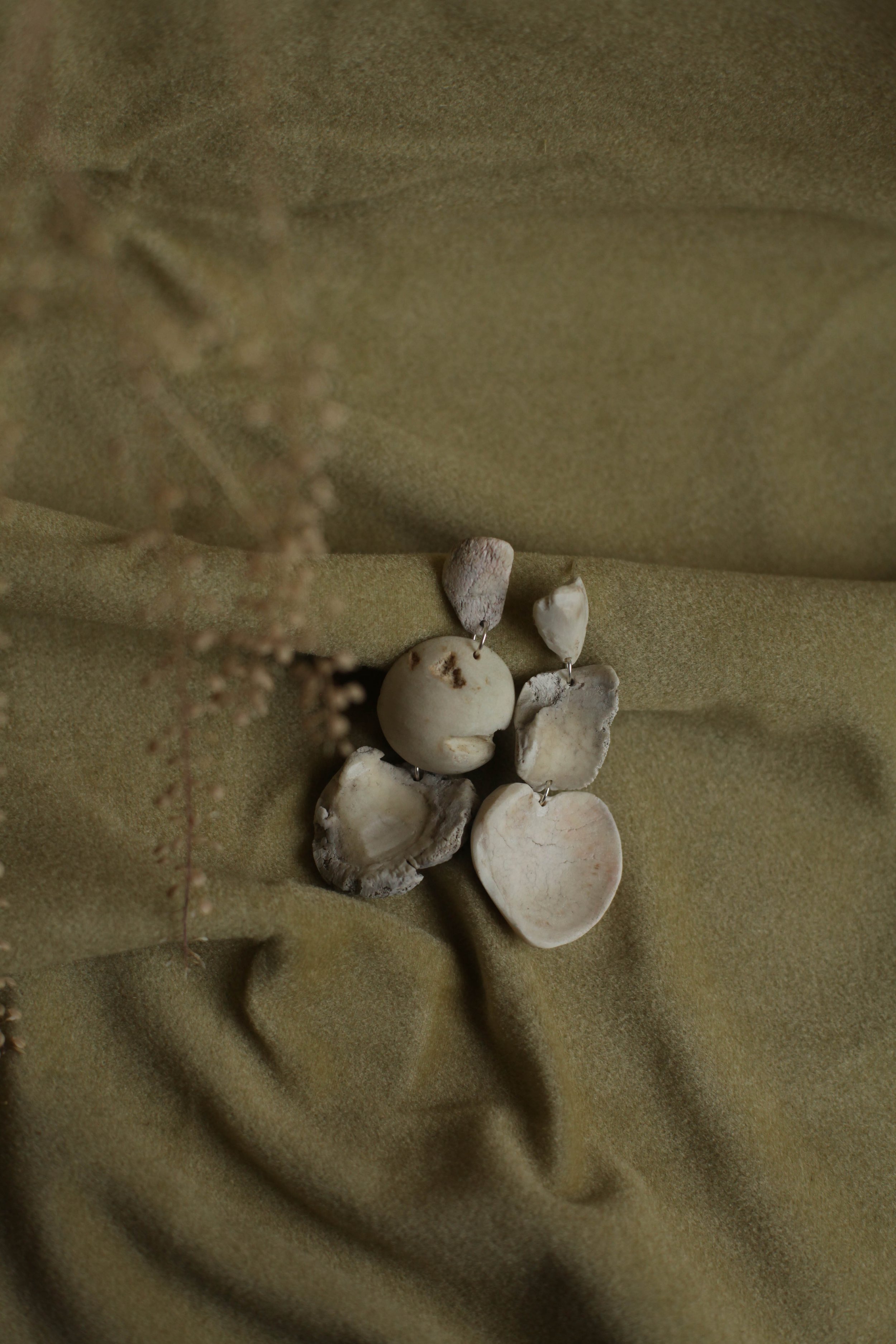 A collection of assorted bones earrings on a green fabric background with blurred dried plant in the foreground.
