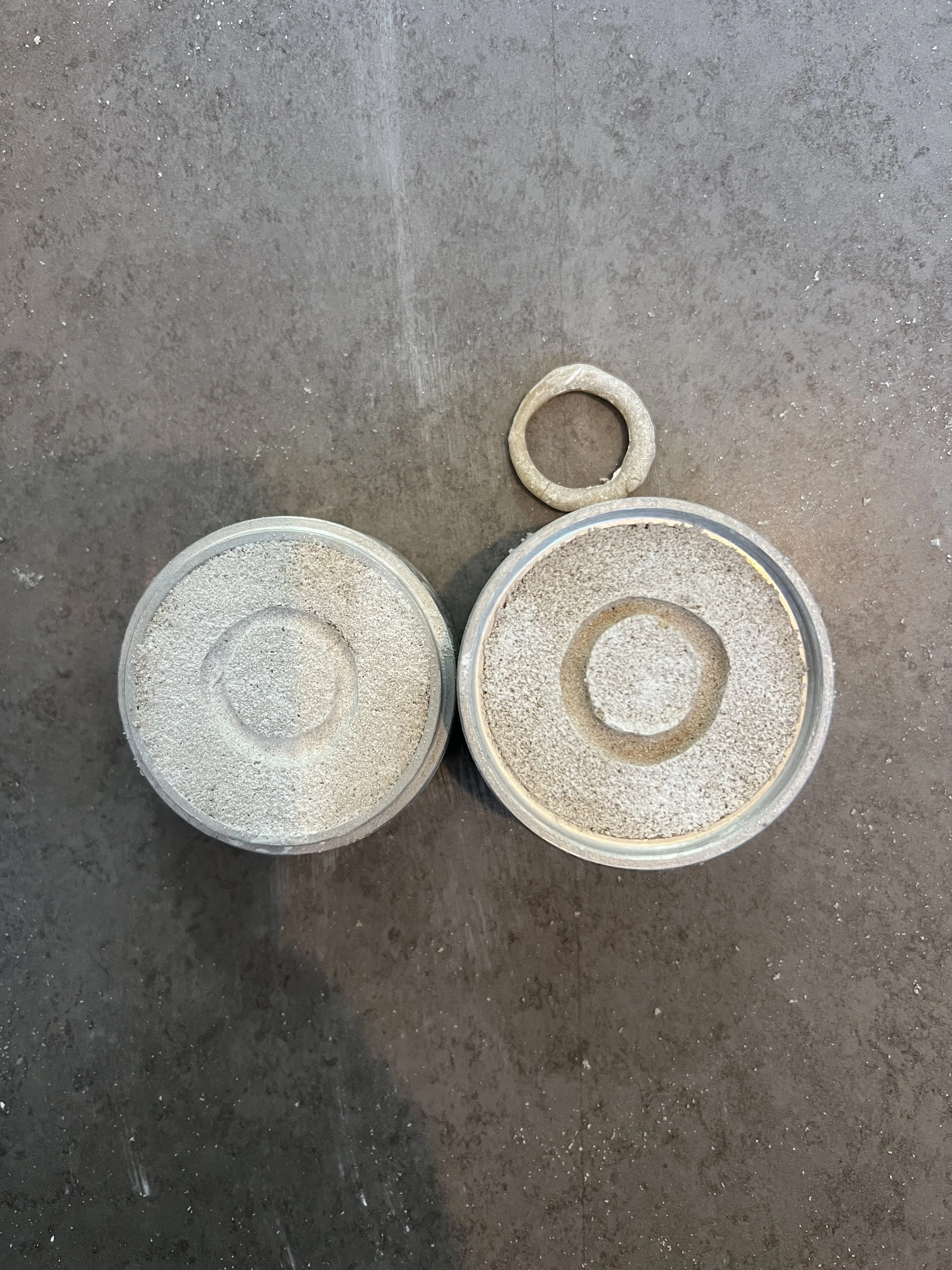 Two containers filled with a granular white substance, with a small ring-shaped mold above them, on a brown surface.