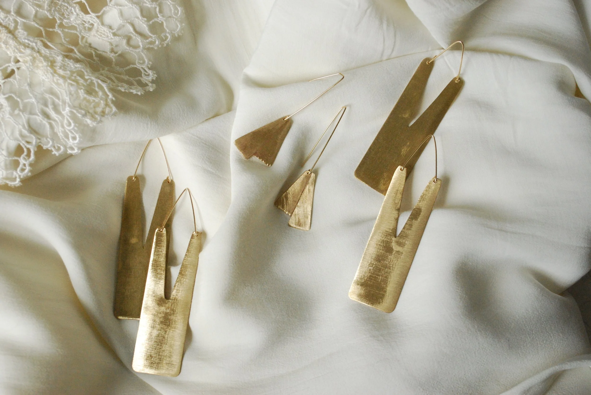 Various gold jewelry pieces, including earrings and necklaces, displayed on a white fabric background.