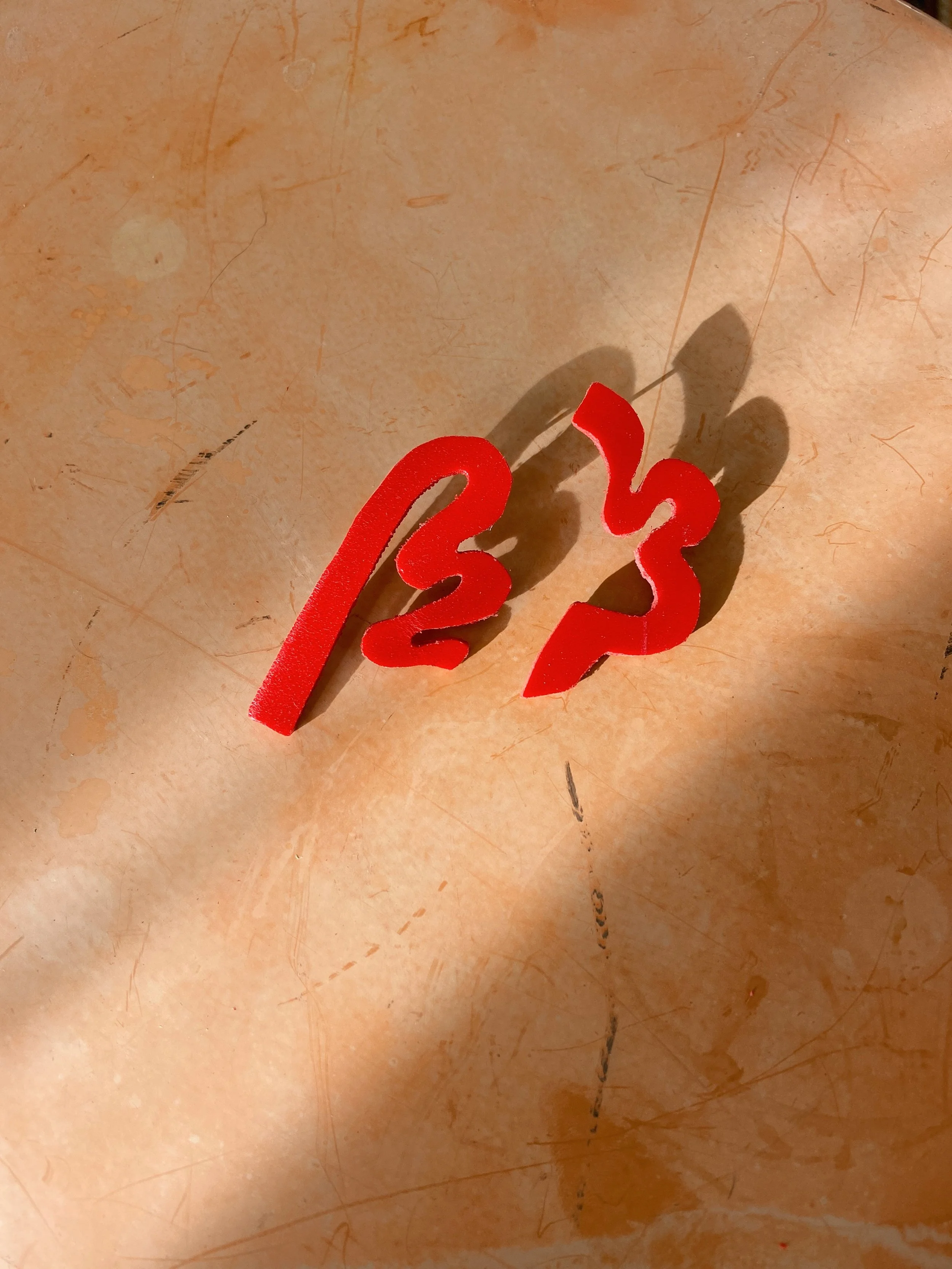 Red acrylic earrings on a beige surface with shadows.
