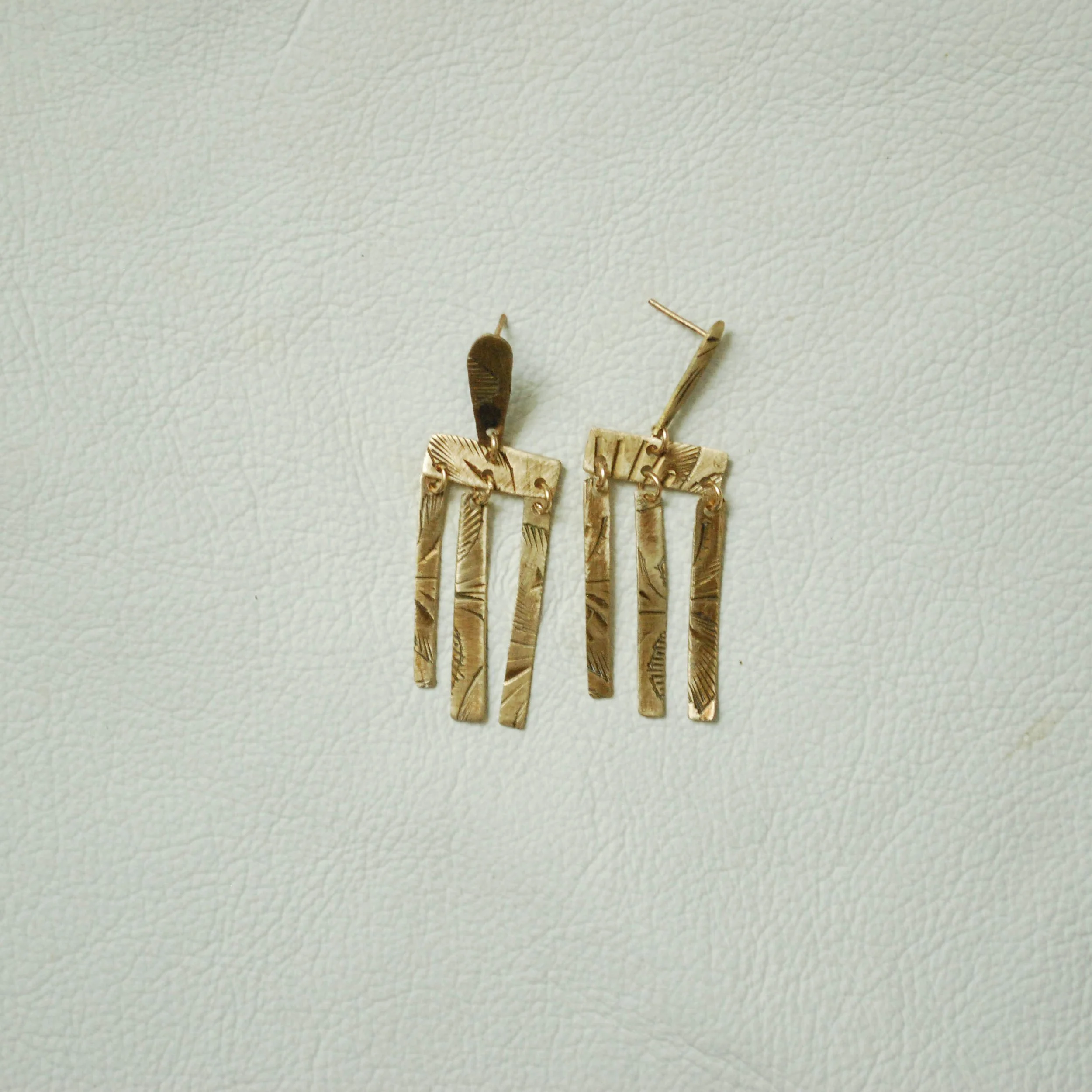 Brass geometric dangle earrings with textured rectangular shapes on a white textured background.