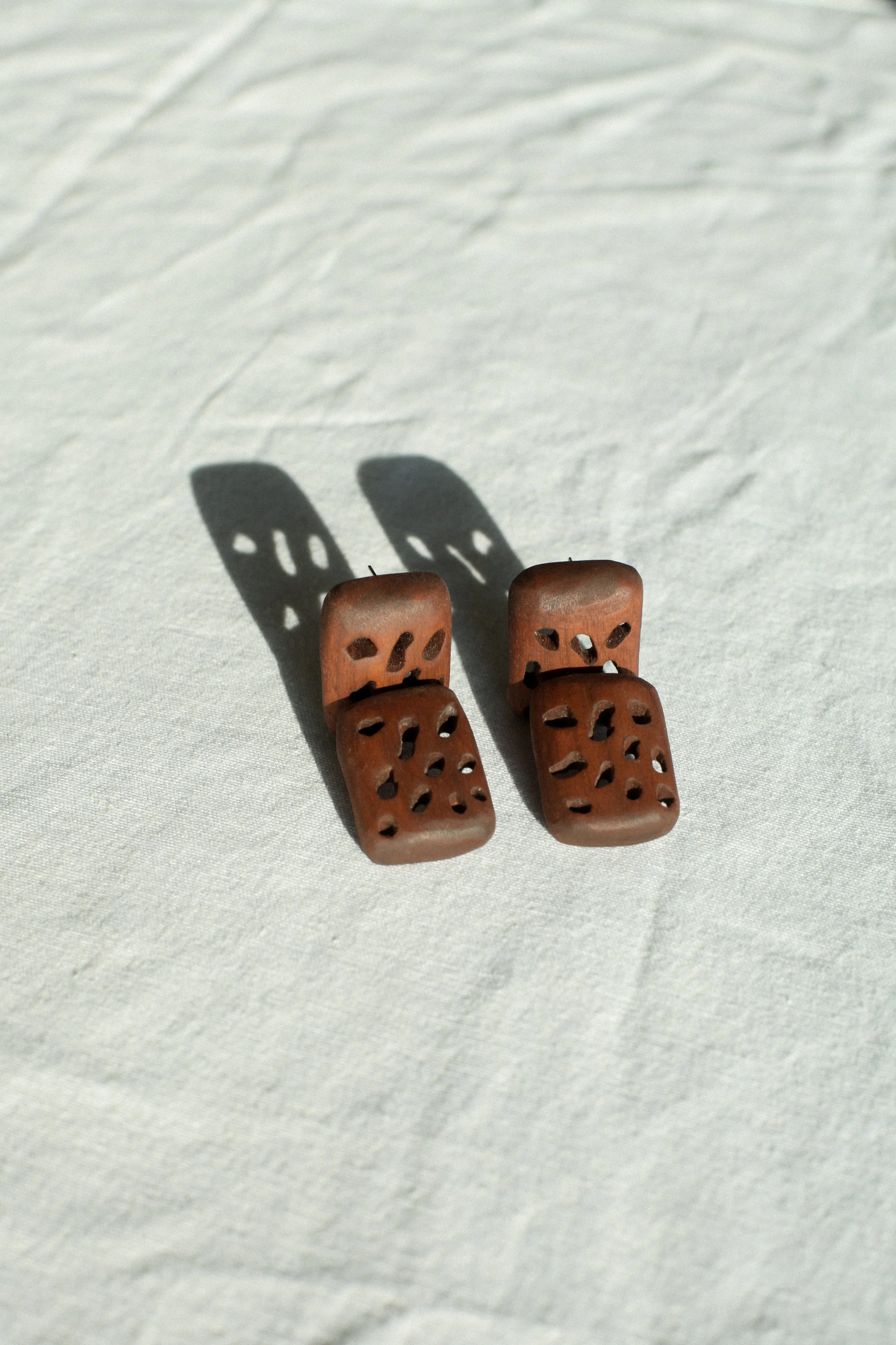 Two hand carved wooden earrings made from repurposed chair on a light surface, casting shadows.