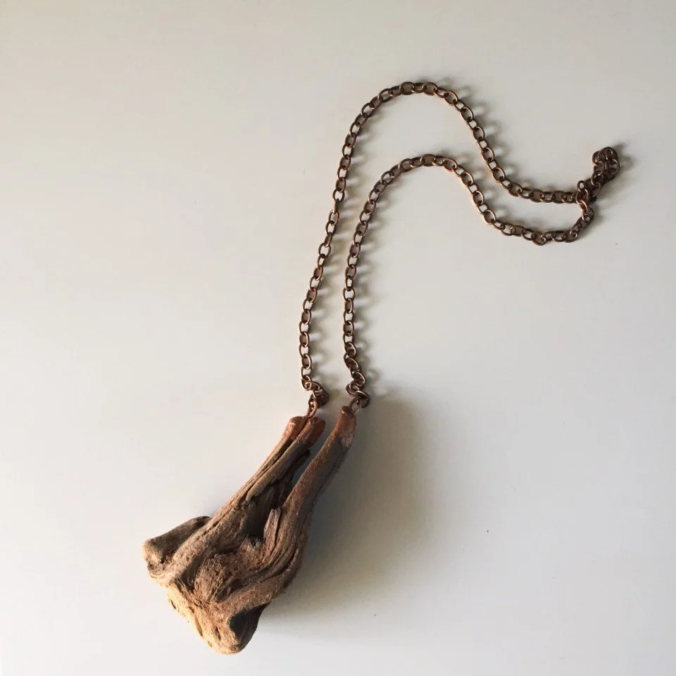 A necklace with a piece of driftwood on a chain is displayed on a white background.