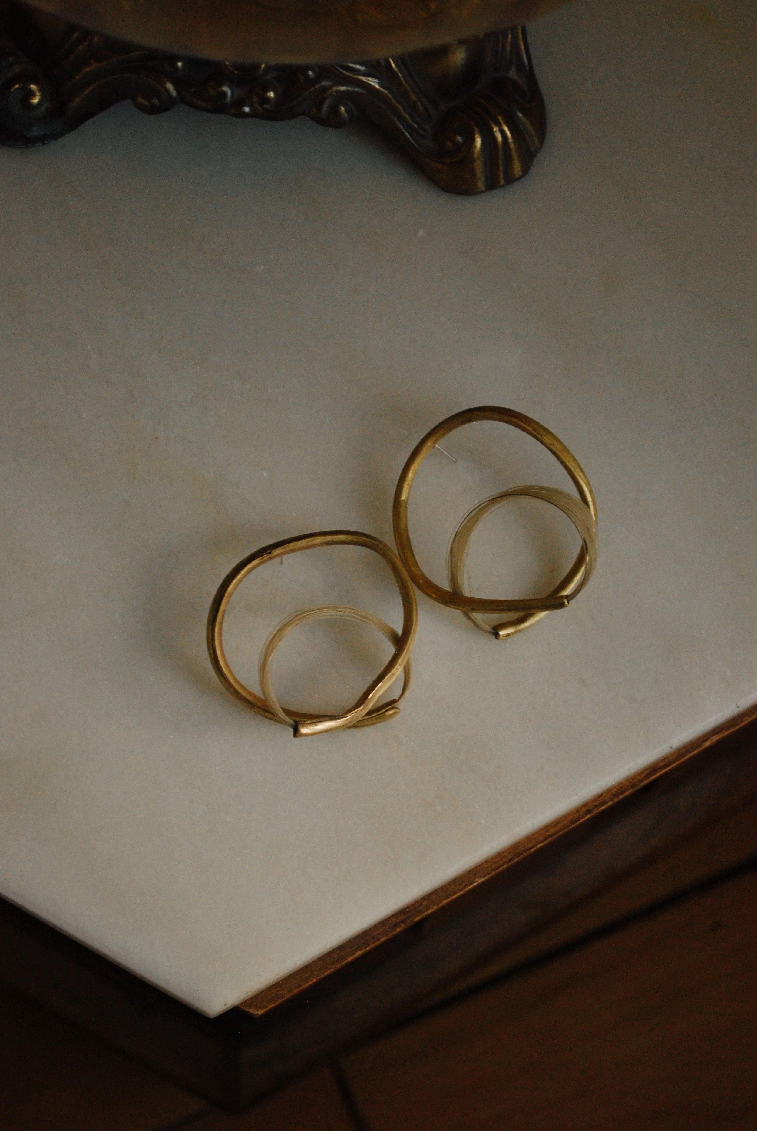 Pair of gold hoop earrings placed on a light-colored surface, with part of a decorative object visible at the top.