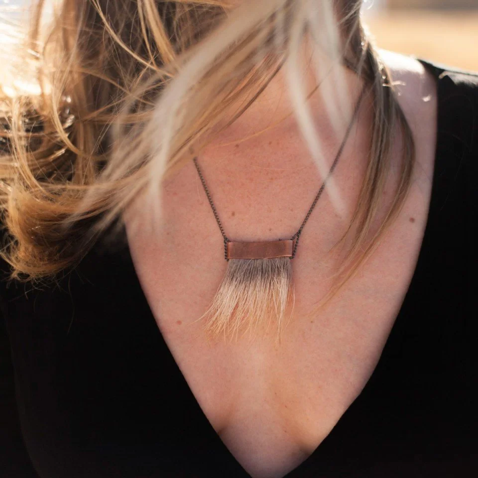 A woman wearing a necklace with a rectangular metal pendant and a hairpiece that extends downward from the pendant.