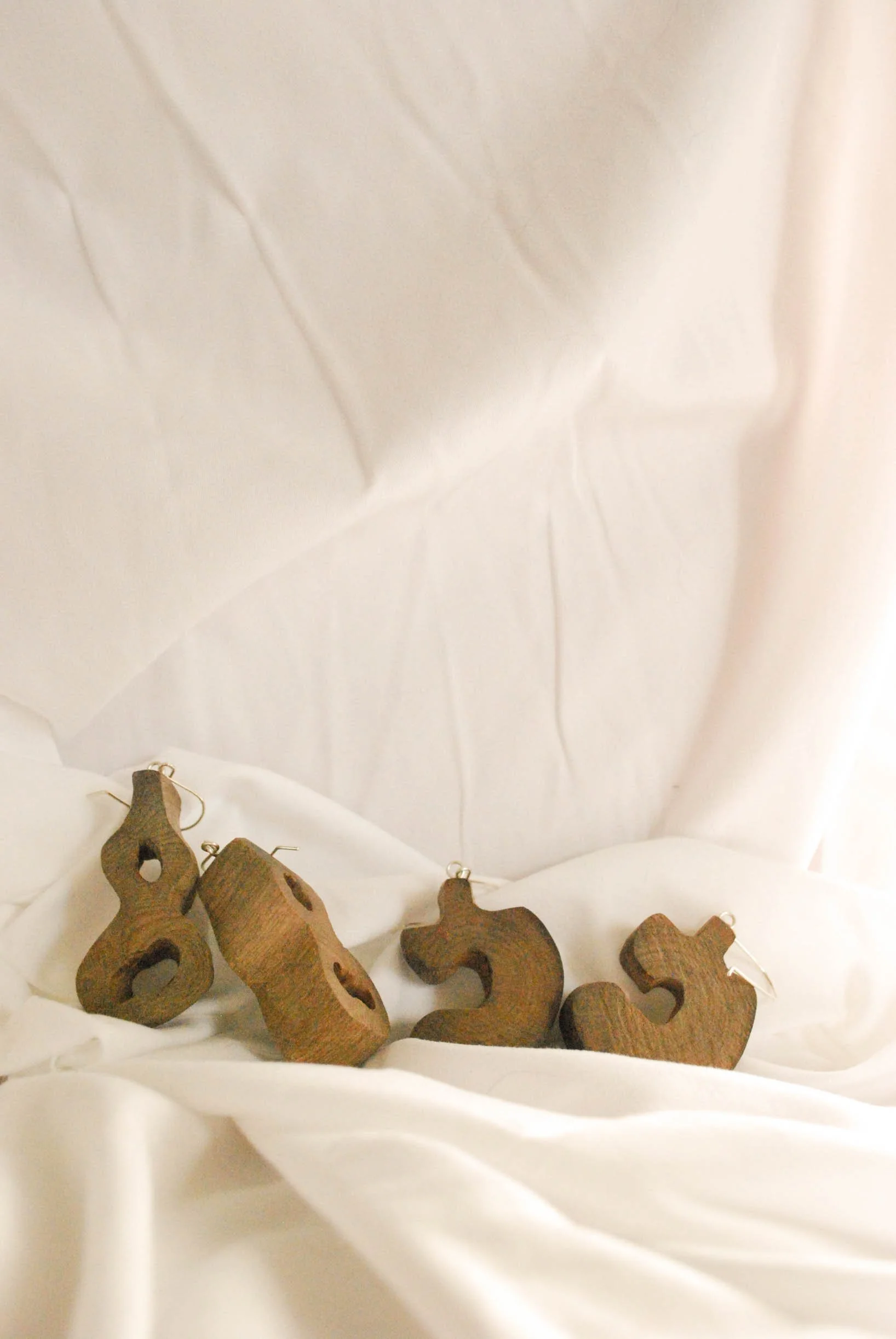 Four wooden earrings carved into different abstract shapes arranged on a white fabric background.